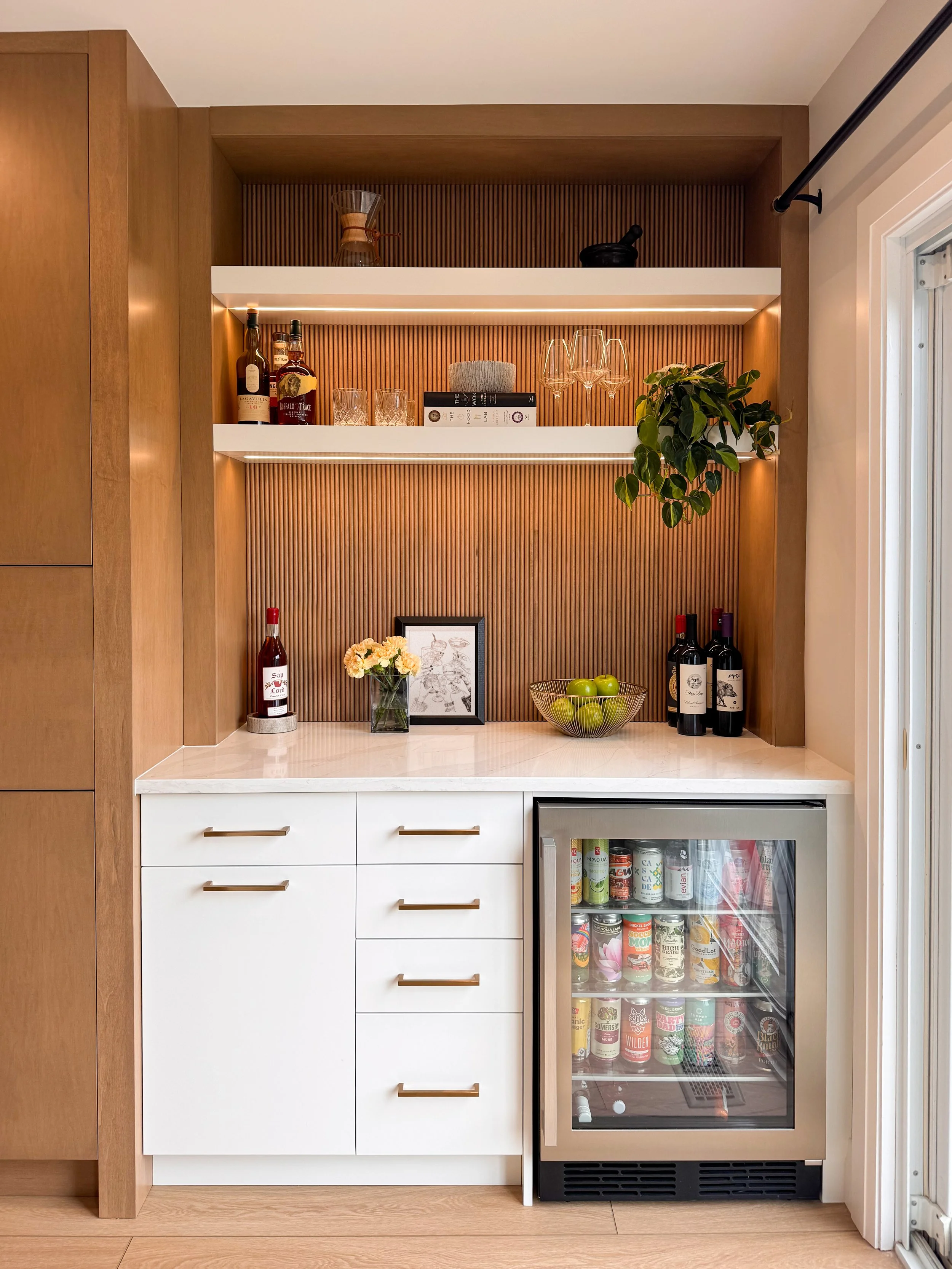 A modern built-in beverage bar with custom wood-slat back paneling, integrated under-shelf lighting, white cabinetry, and a beverage fridge from a home renovation project in Waterloo.