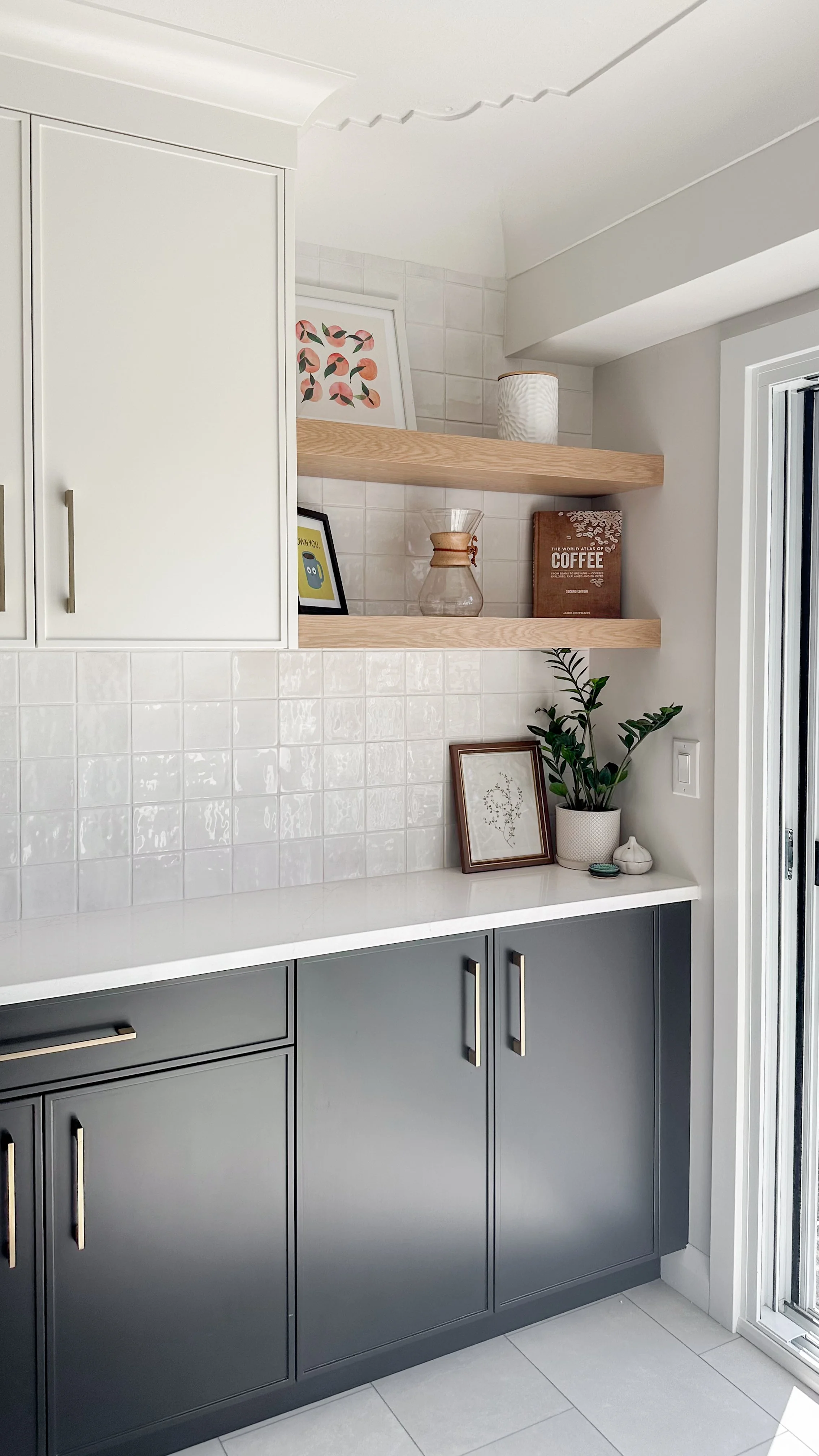 To keep the main workspace totally clear, we designed this dedicated coffee and beverage station. Deep charcoal base cabinets and natural wood floating shelves pop beautifully against the glossy zellige-style backsplash.