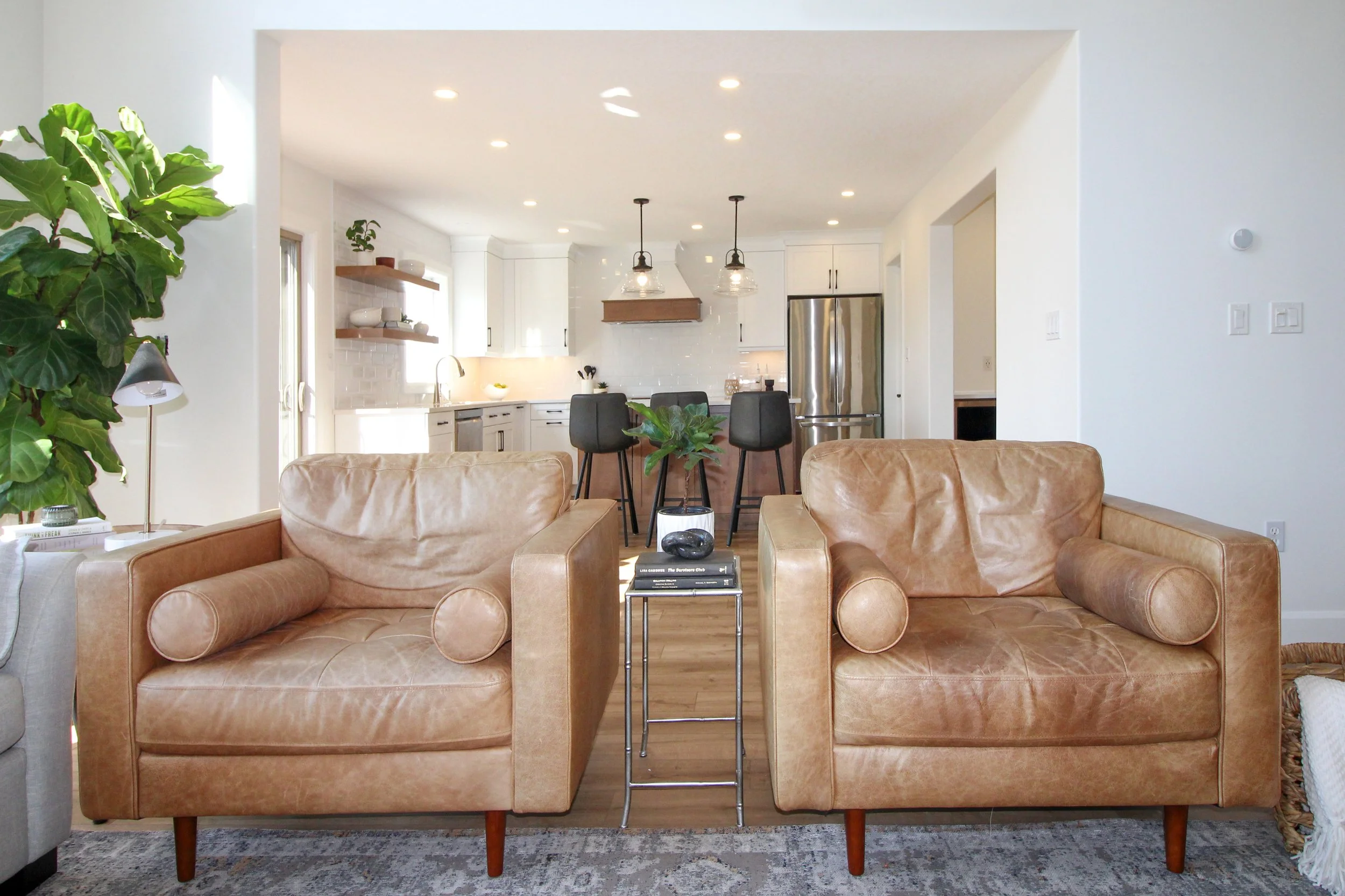 Bright open-concept main floor renovation in Kitchener-Waterloo featuring a modern white kitchen with open wood shelving, stainless steel appliances, and a seamless view from the living room.