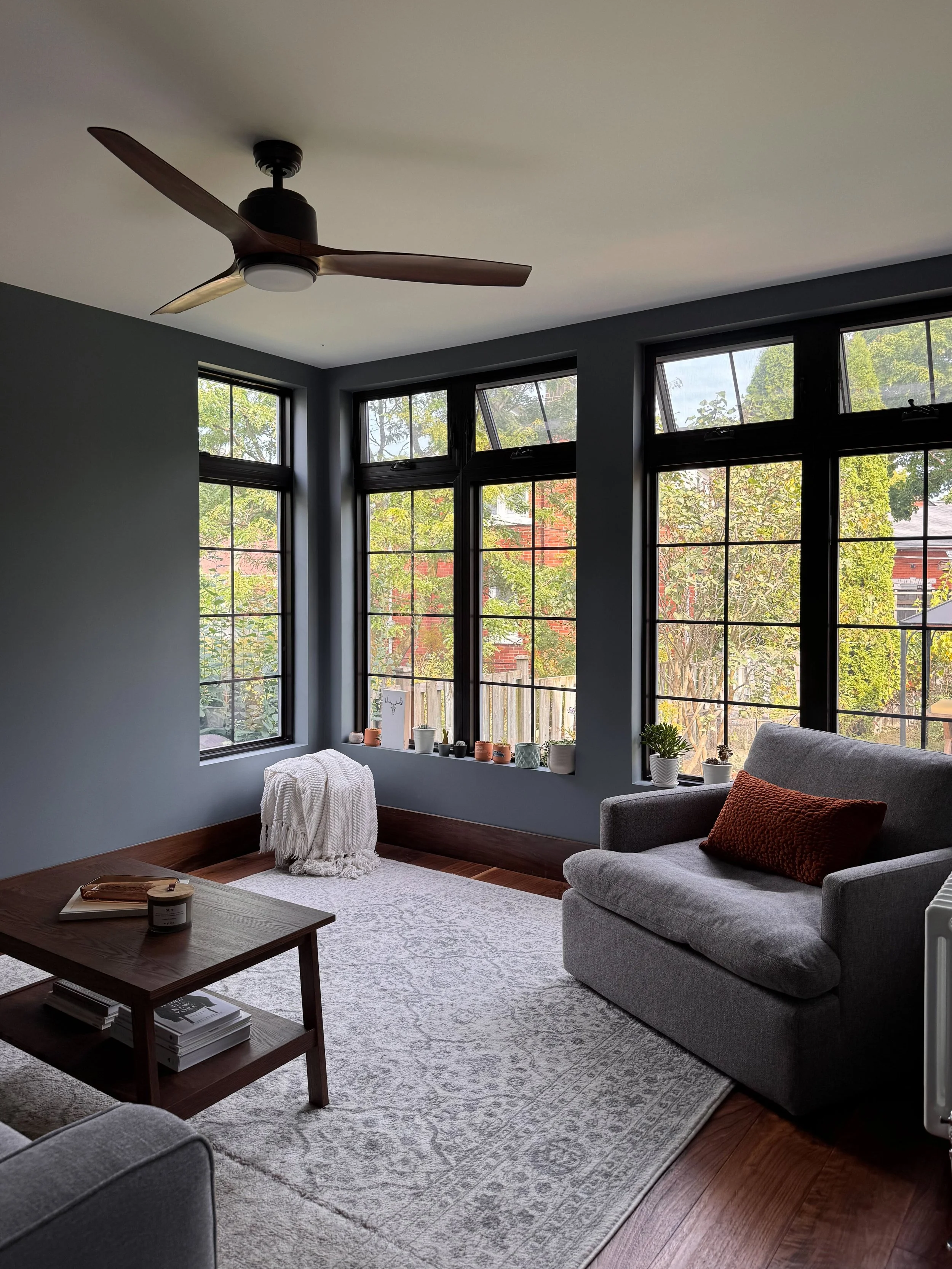 Modern sunroom design with dark charcoal walls, large black-framed windows, and a wood ceiling fan.