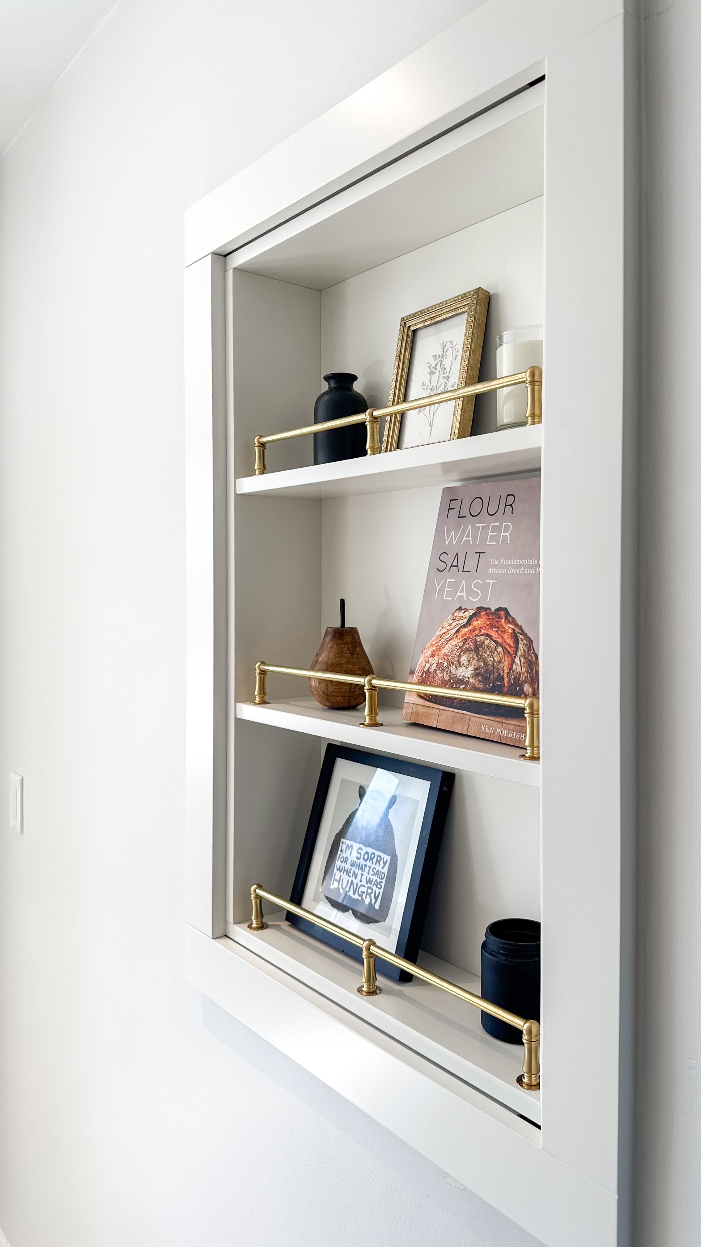 Built into a wall cavity discovered during demo, this custom shelf serves as both a staging zone for cookbooks and decor, cleverly concealing extra bulk storage behind it.