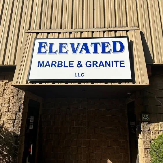 Sign for Elevated Marble & Granite LLC mounted on a building exterior with beige siding and brick walls.