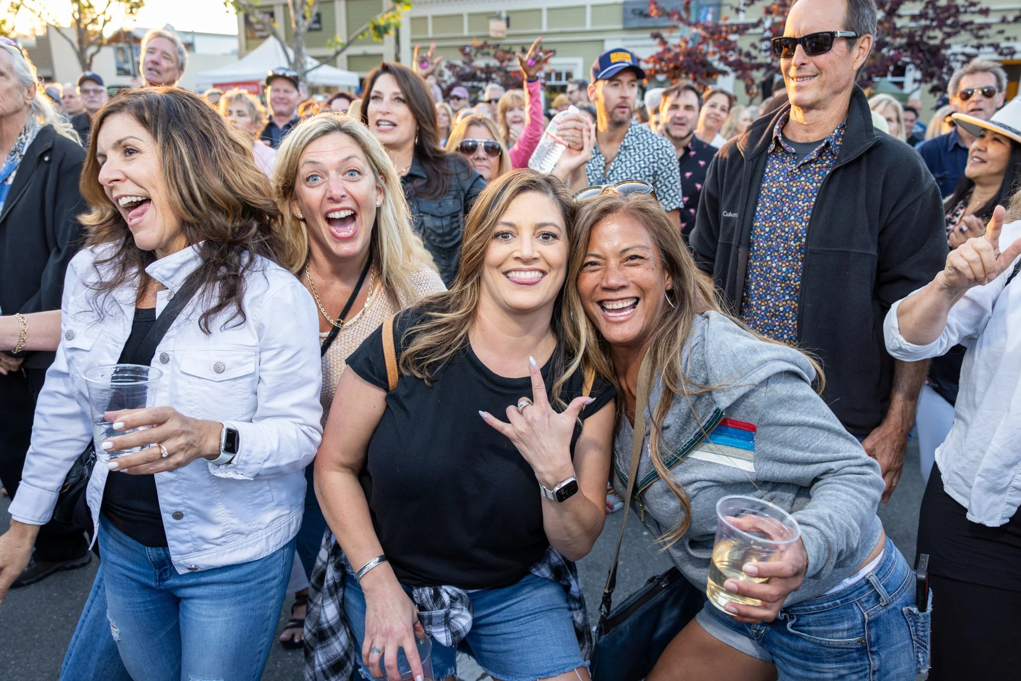 Group of people enjoying Rock the Block, smiling, and having fun with drinks, some making cheerful gestures, in Downtown Novato California.