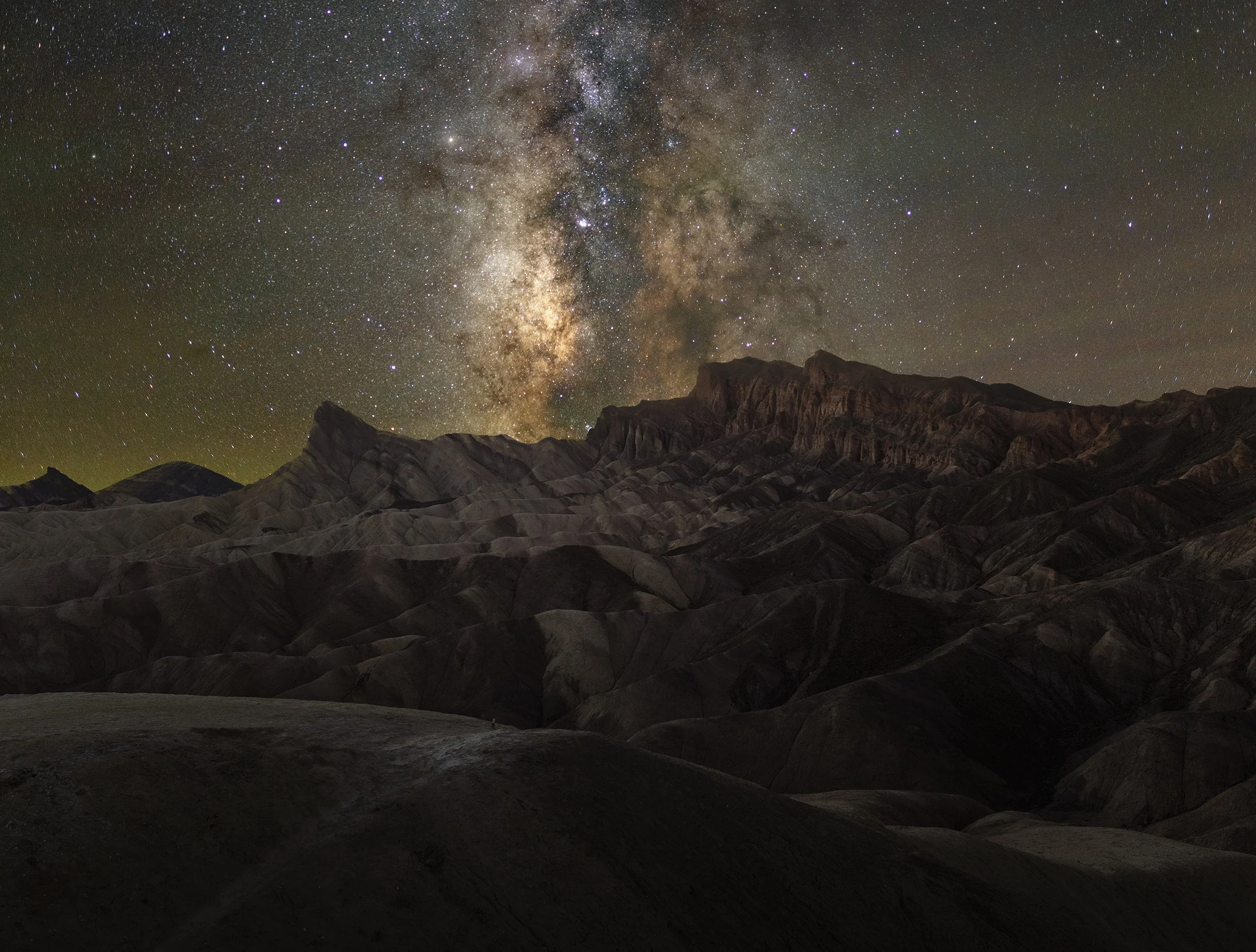 Nighttime desert landscape with rugged, dark hills under a star-filled sky and the Milky Way galaxy prominently visible.