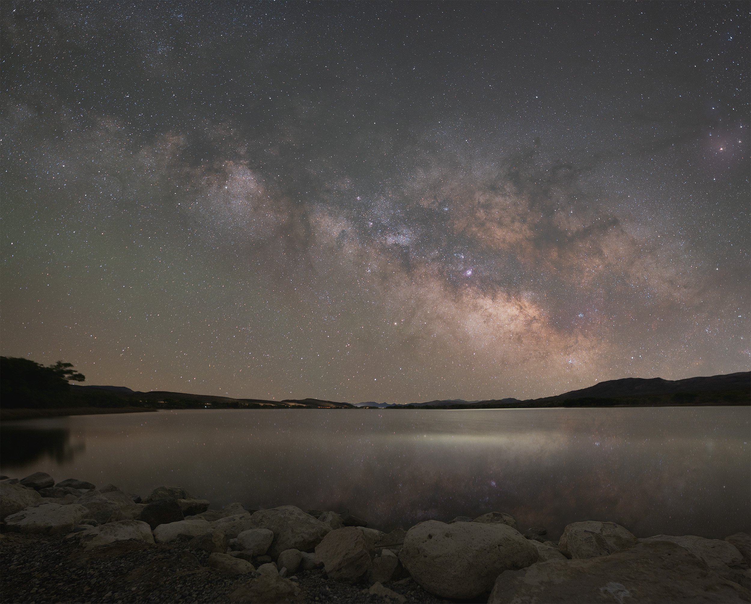 The Milky Way core - our - galaxy, and a star filled night sky rising over a smooth calm lake