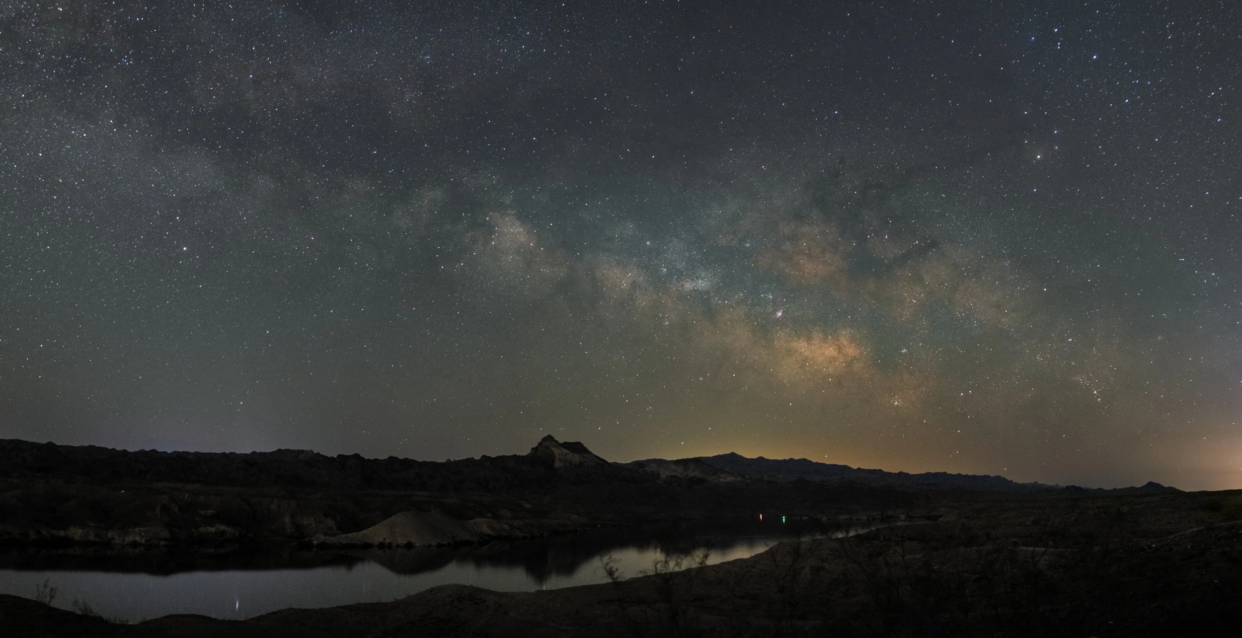 A horizontal Milky Way and the colors of the night sky rising over a desert mountain landscape and river