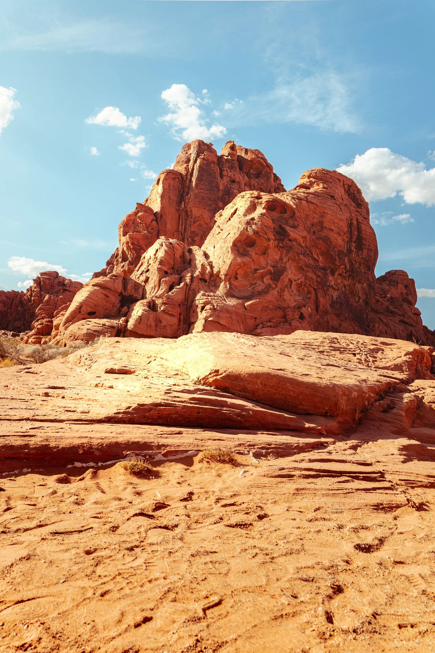 Large red sandstone rock formations in a desert landscape under a blue sky with scattered white clouds.