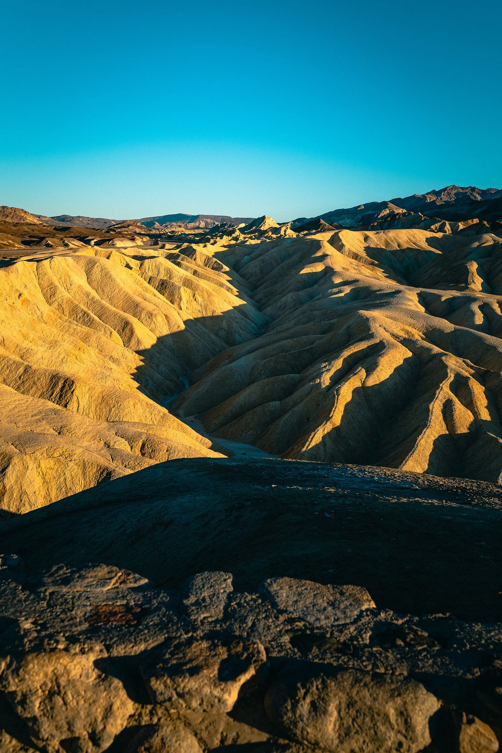 Sunlit $andy yellow and tan layered hills in a desert landscape under a clear blue sky.
