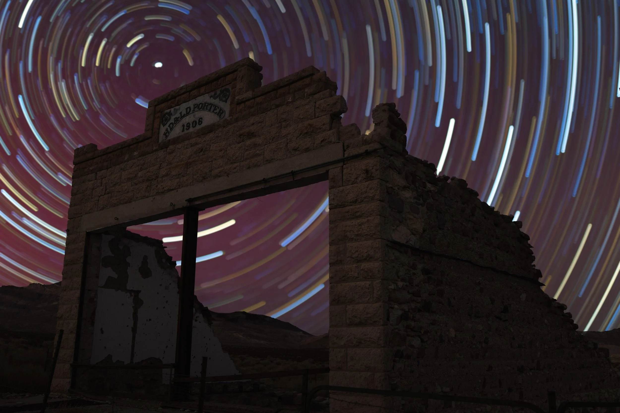 Colorful circular star trails in the red sky of an Aurora Borealis set against the ruins of a ghost town