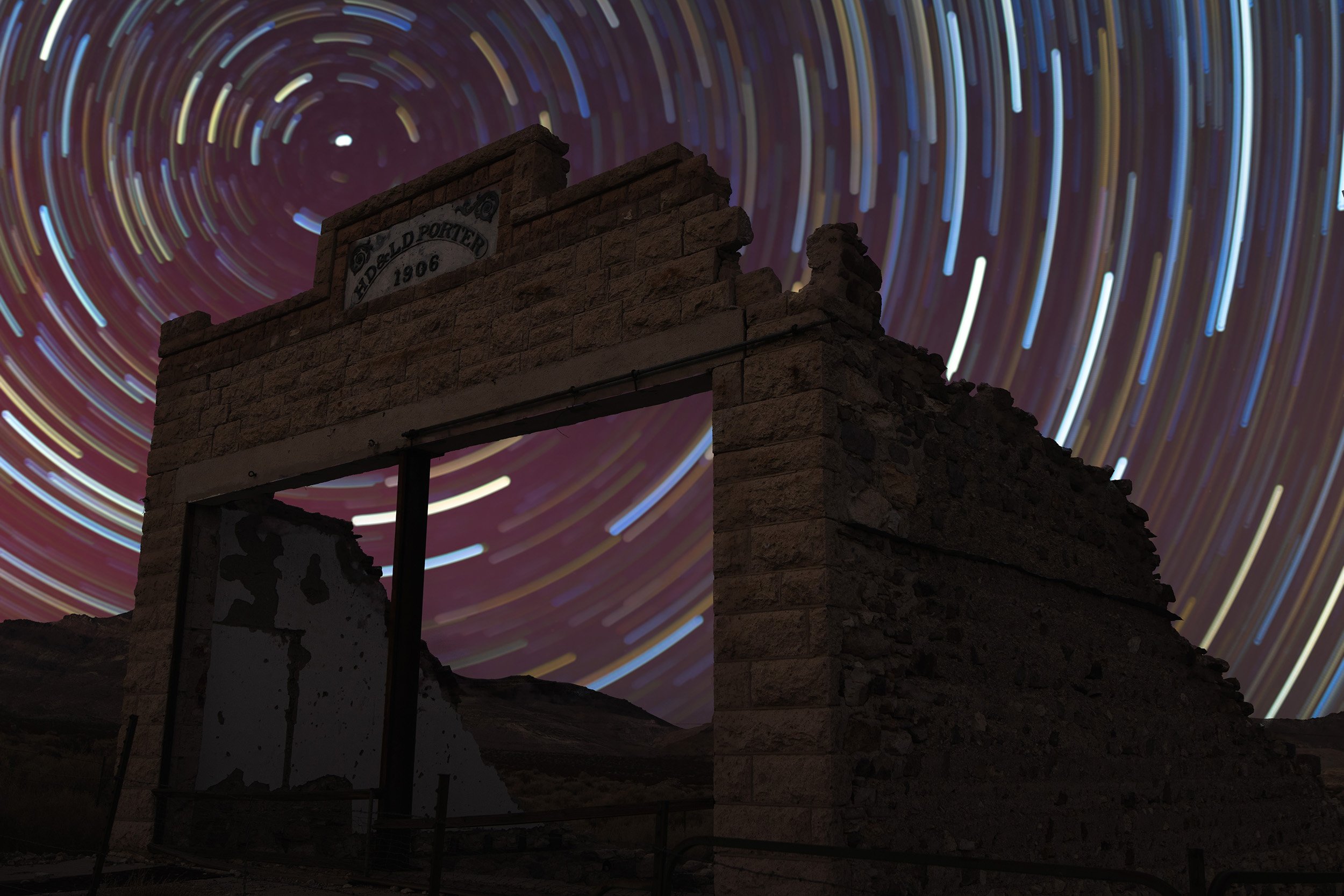 A night sky with star trails over the ruins of an old stone building.