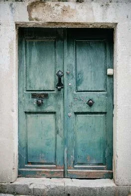 Old green double door with black handle and a mail slot, set in a concrete wall.
