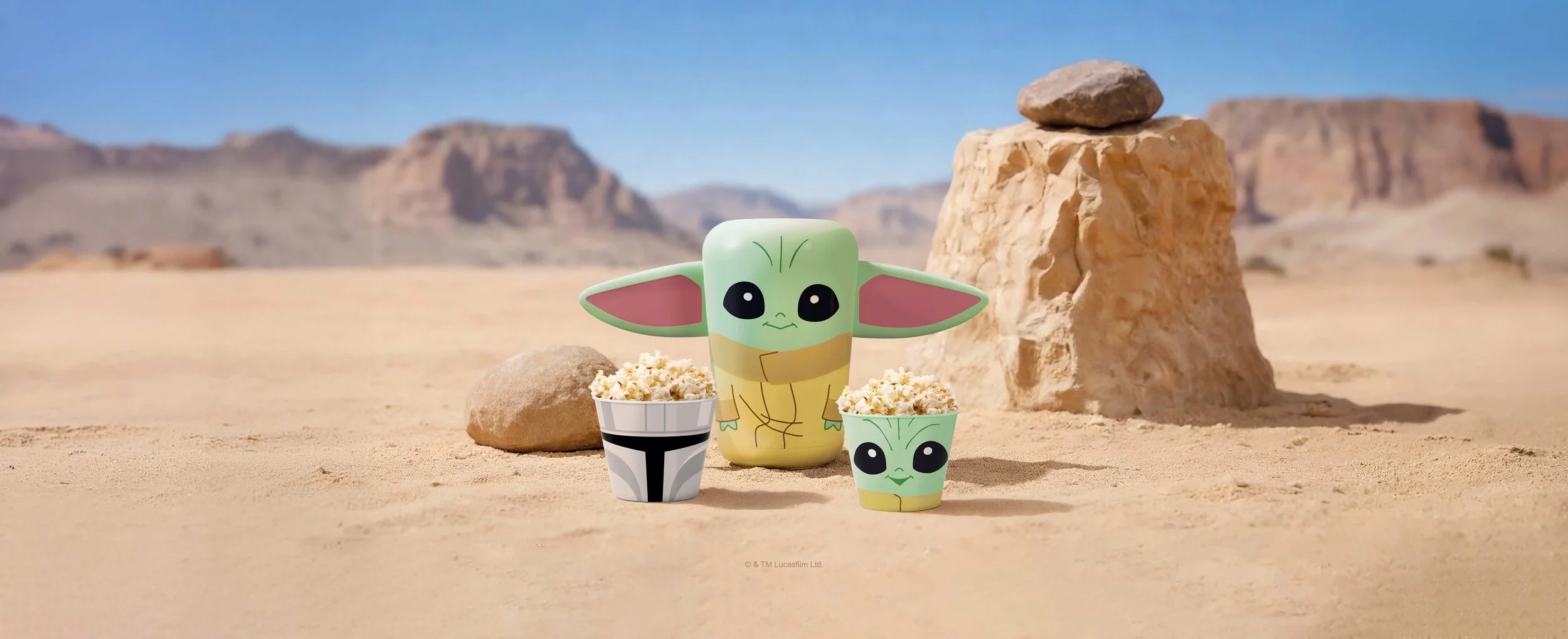 Grogu surrounded by two popcorn bowls with similar facial features, in a desert landscape with rocks and mountains in the background.