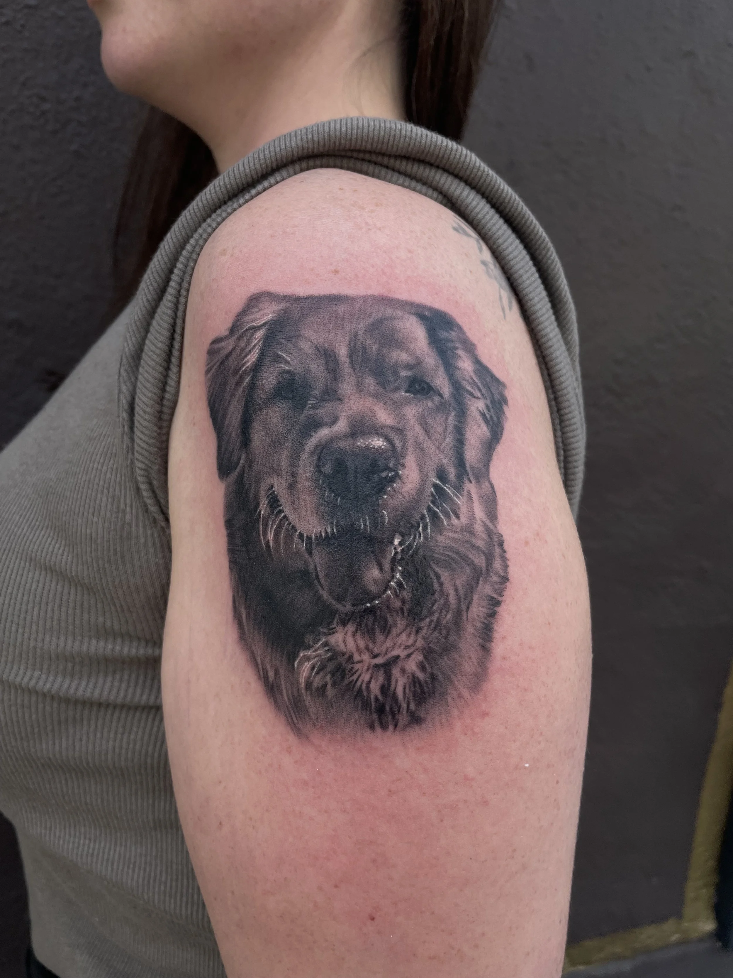 Tattoo of a happy dog's face on a person's upper arm.