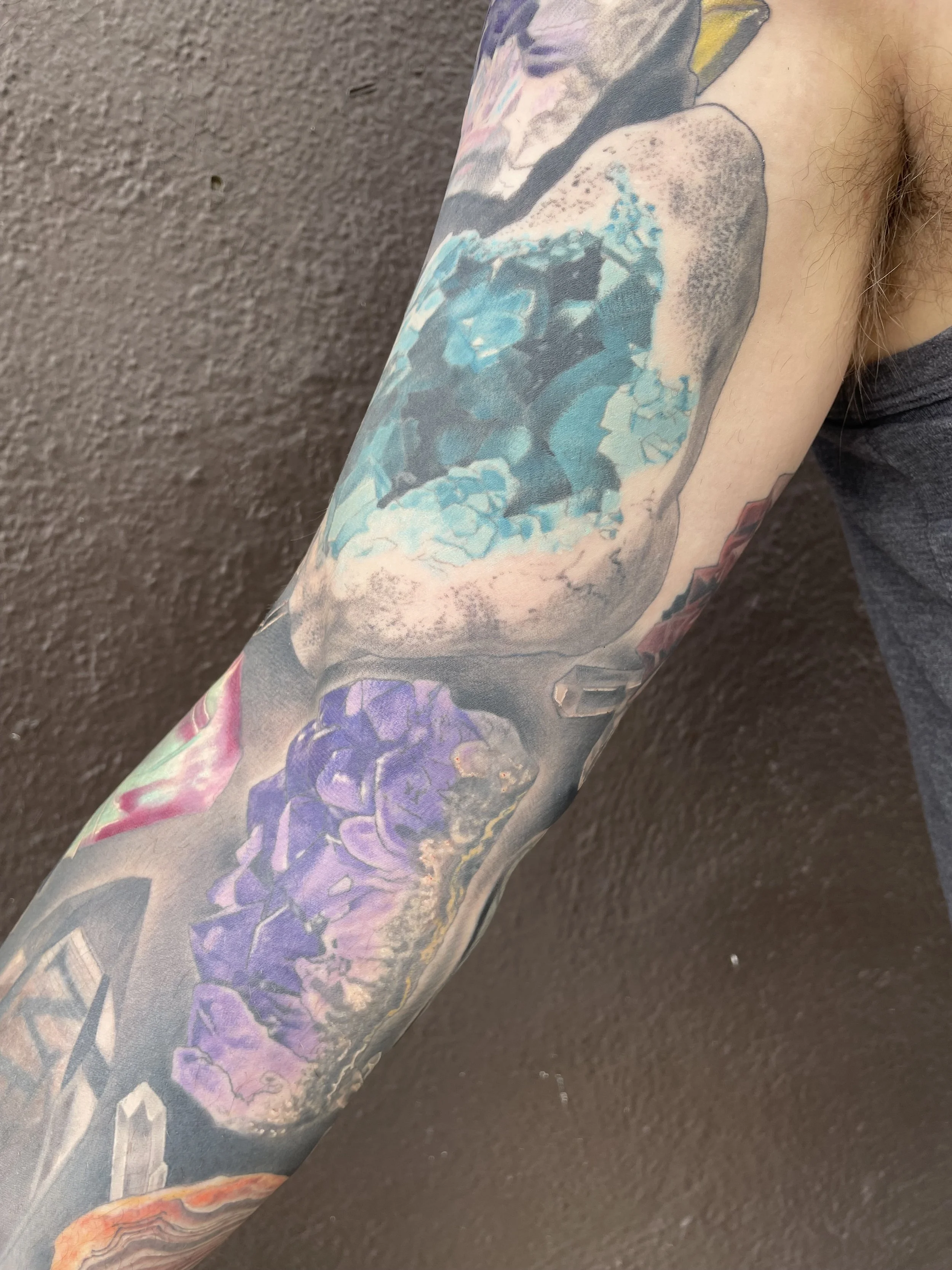Close-up of a person's arm with a colorful tattoo sleeve featuring various abstract and floral designs.