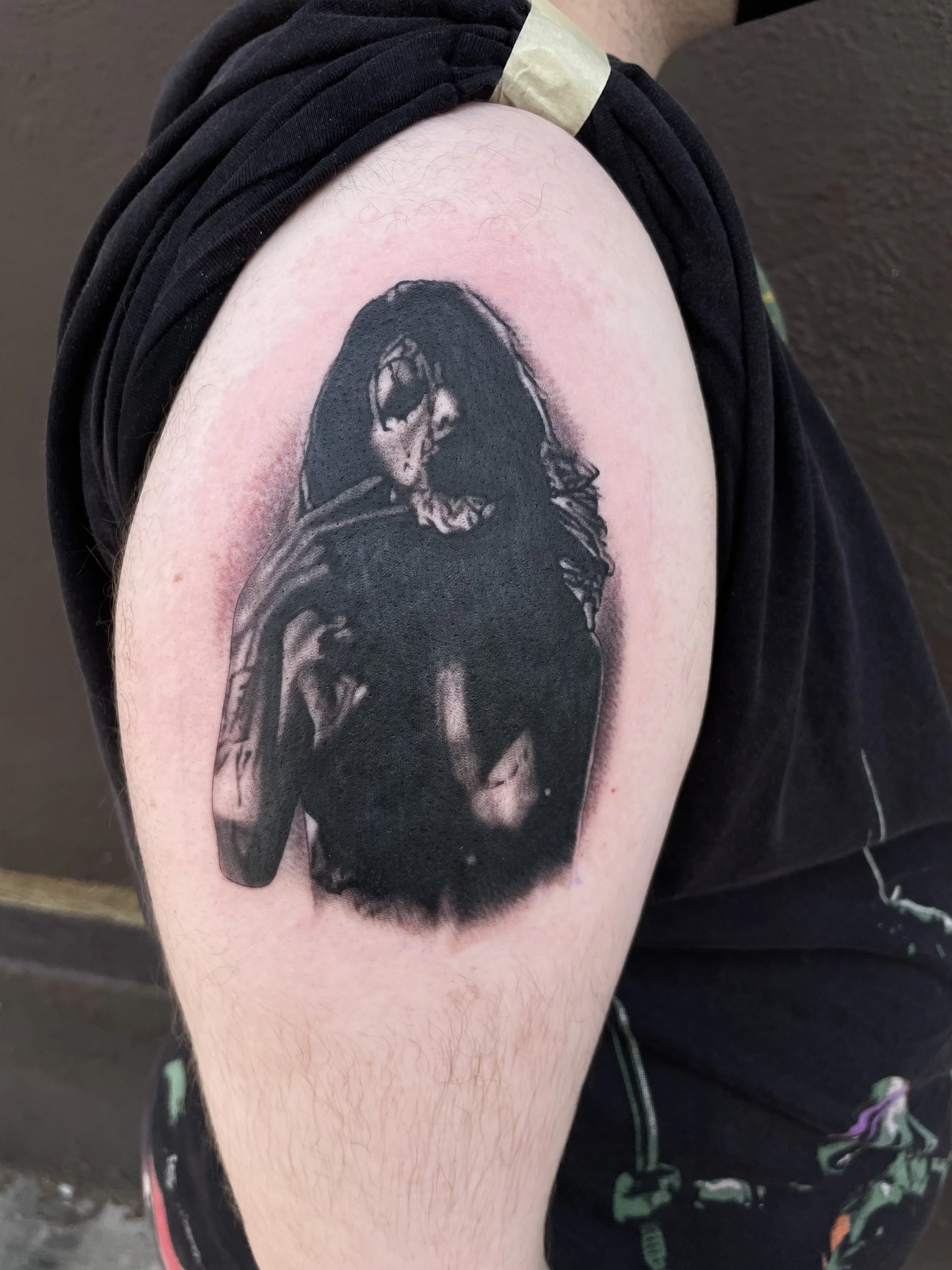 Black and grey tattoo of a woman with long hair and sunglasses, holding a cigarette, on an upper arm.