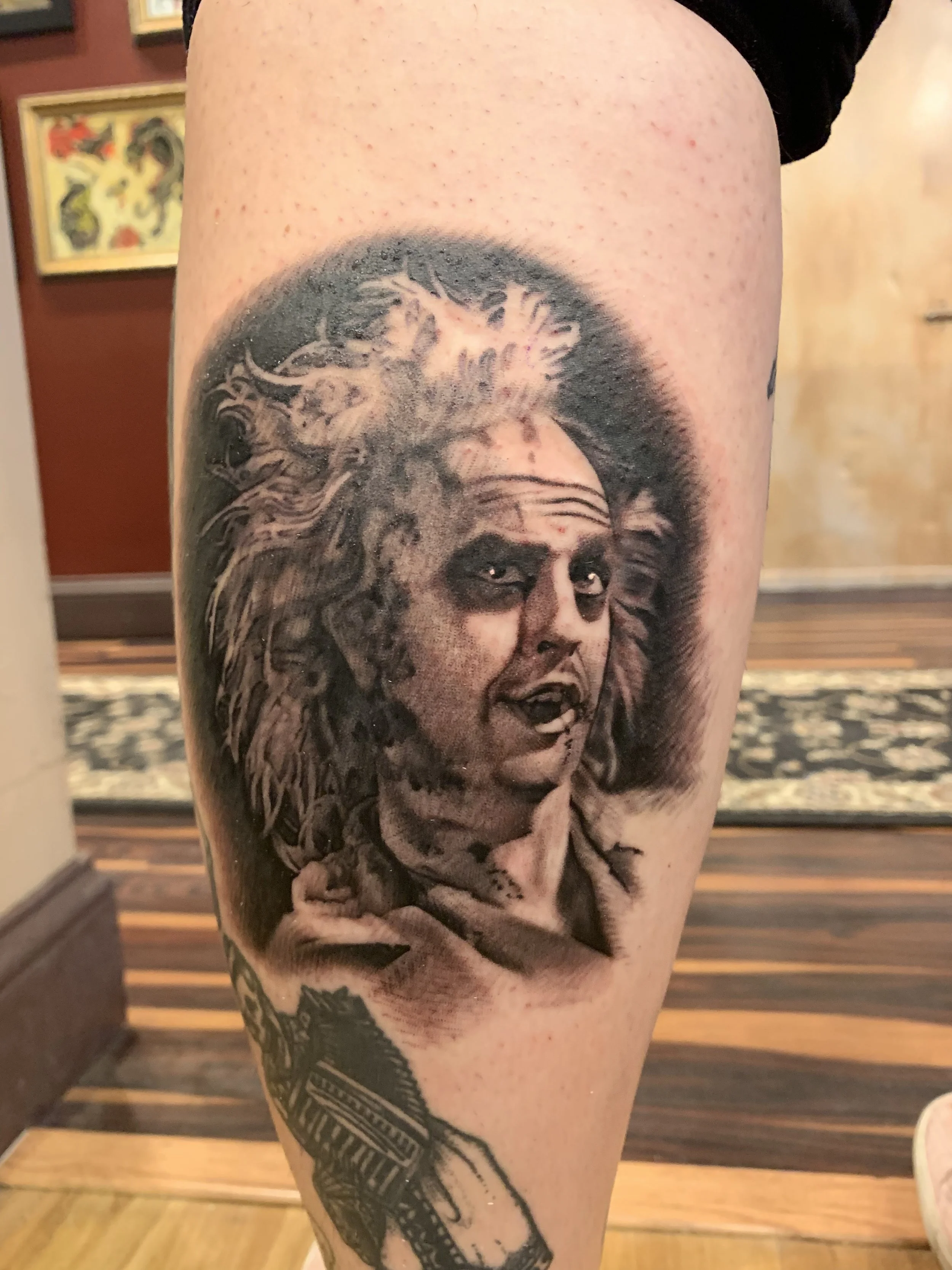 Black and gray tattoo of a woman's face with a lion's mane as hair on a person's thigh.