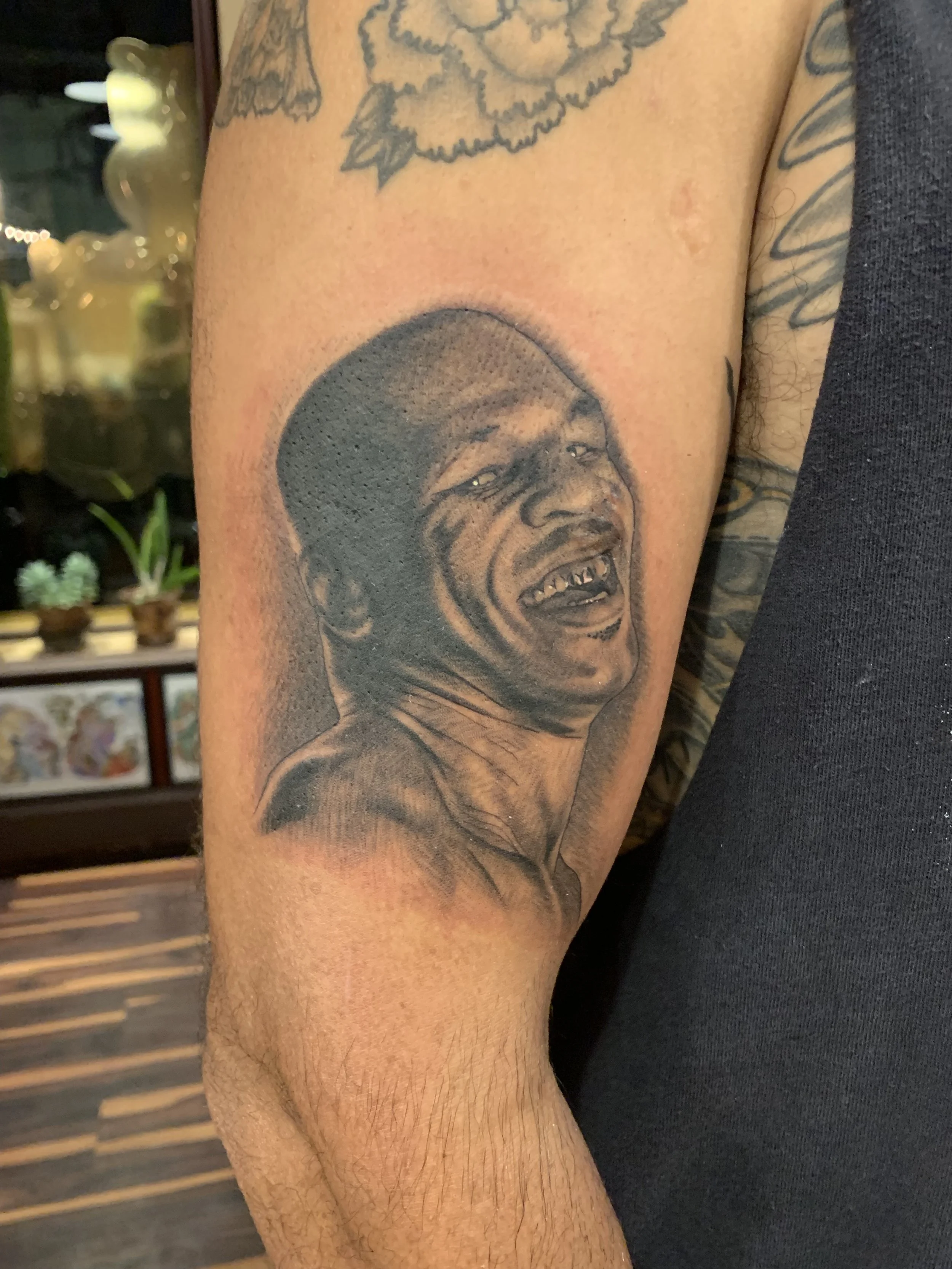 Black and gray tattoo of a laughing man with missing teeth on a person's upper arm.