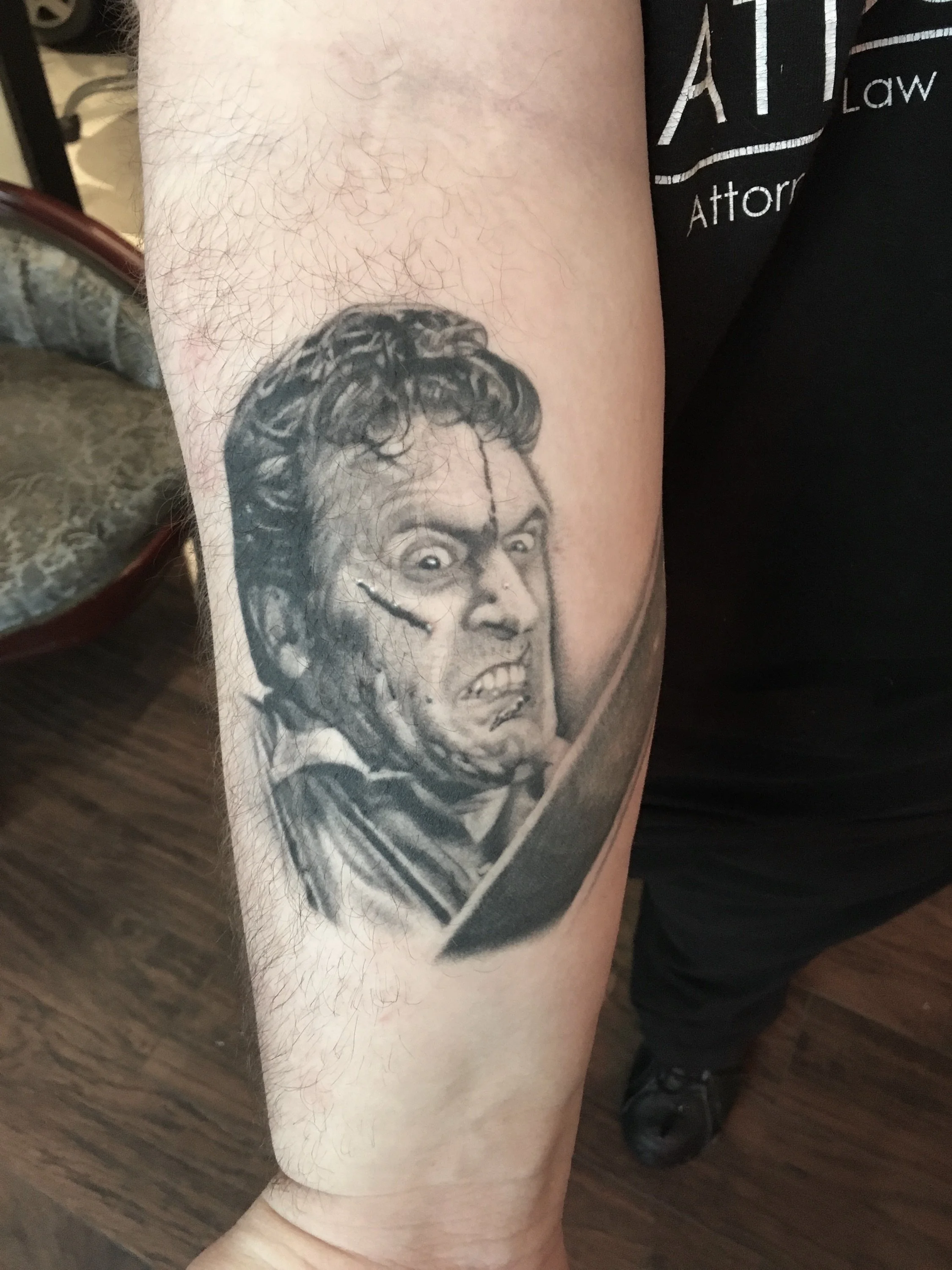 Black and gray tattoo of a zombie with a distorted face, visible wounds, and grimacing expression on the person's upper arm.