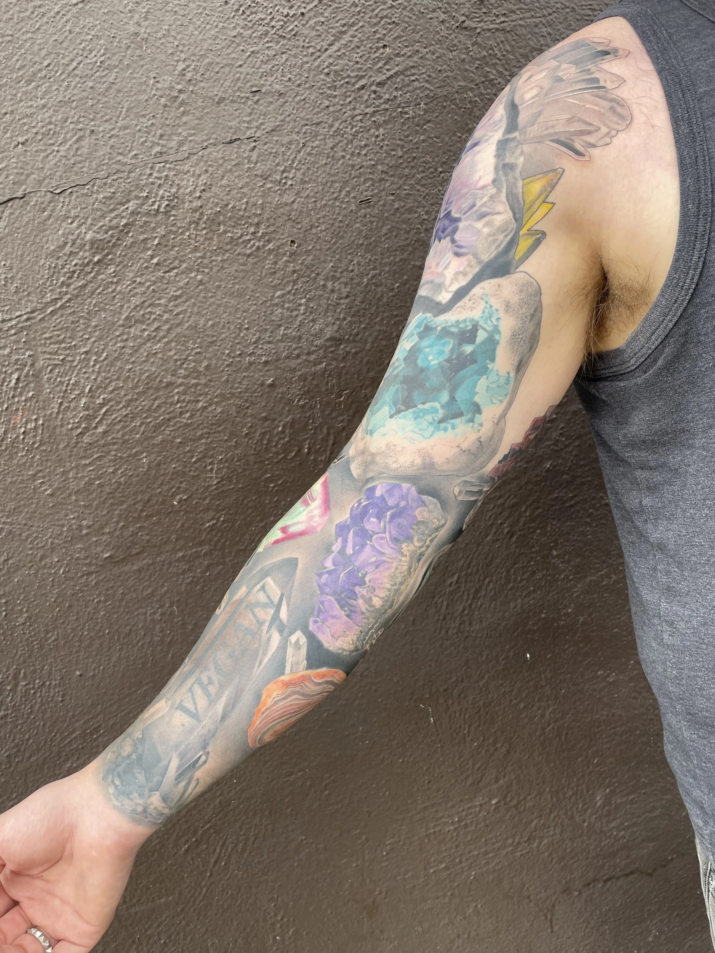 Colorful tattoo sleeve featuring various designs including a mountain landscape, purple flowers, and geometric shapes on a person's arm.