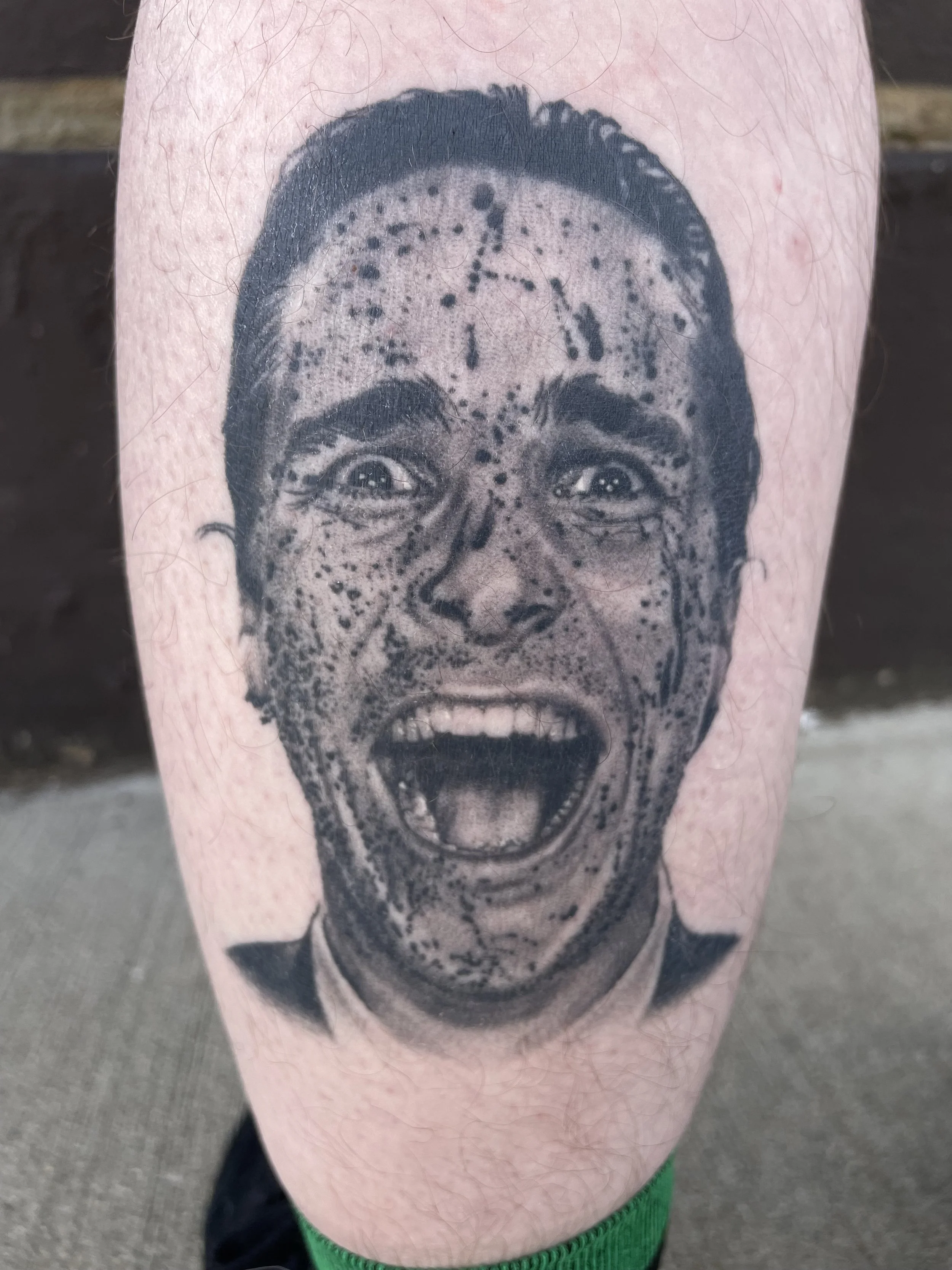 A tattoo on a person's leg depicting a black and gray portrait of a woman with an expressive face, open mouth, and messy hair. The woman appears to be screaming or yelling.