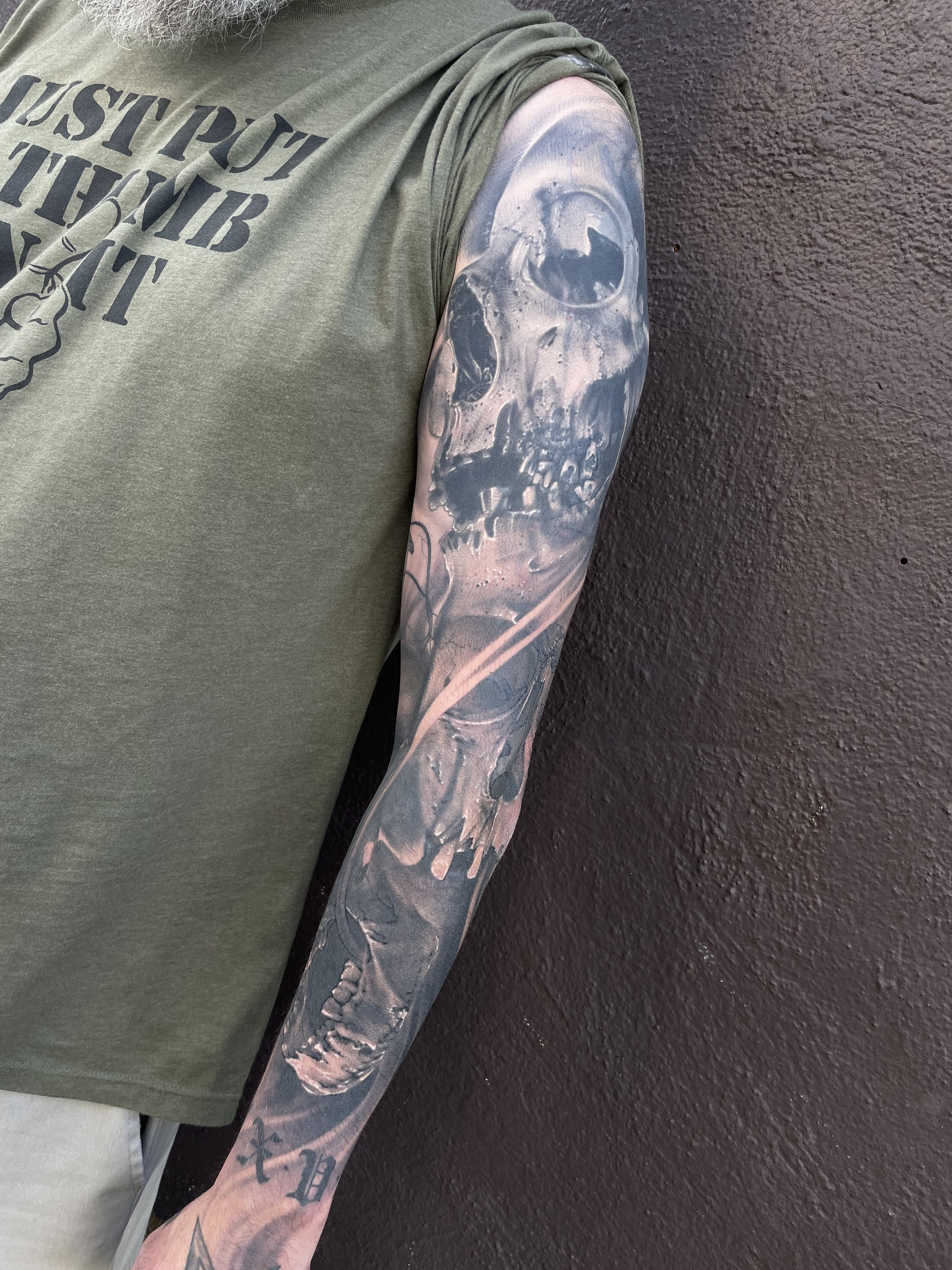 Tattoo of a skull on a person's arm, with detailed shading and realistic features, against a dark background.