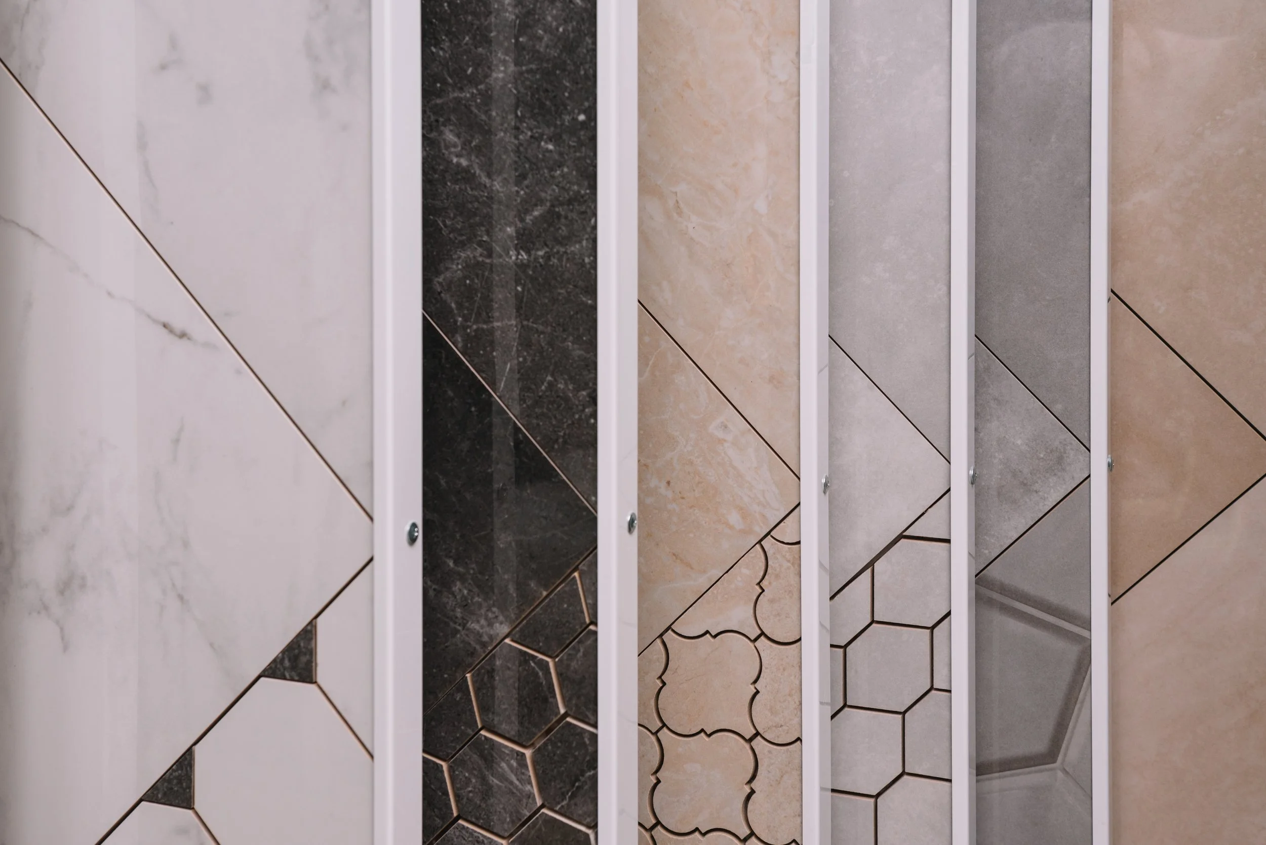 Display of various tile samples in different colors and patterns behind a white frame stand.