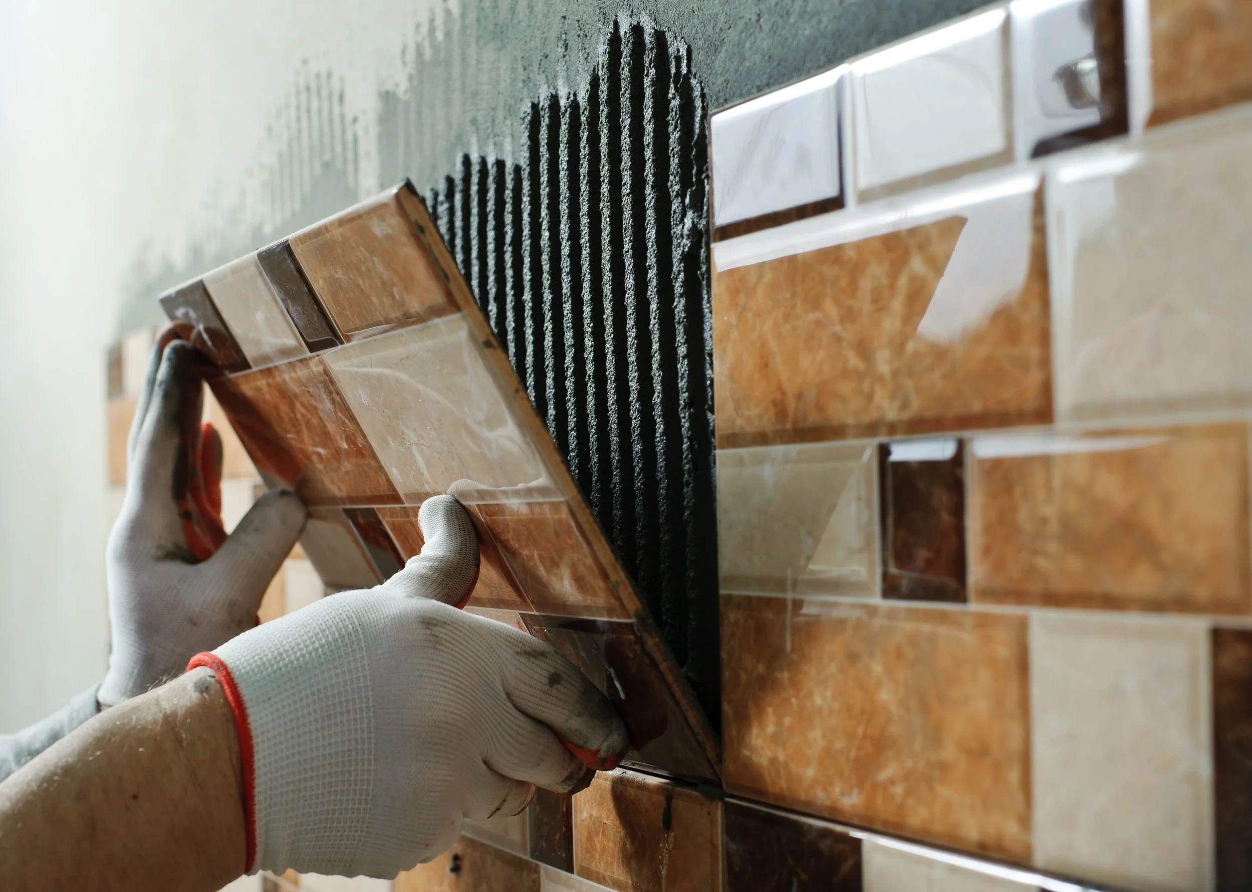 Person installing or replacing decorative ceramic wall tiles in a bathroom or kitchen, wearing white gloves for protection.
