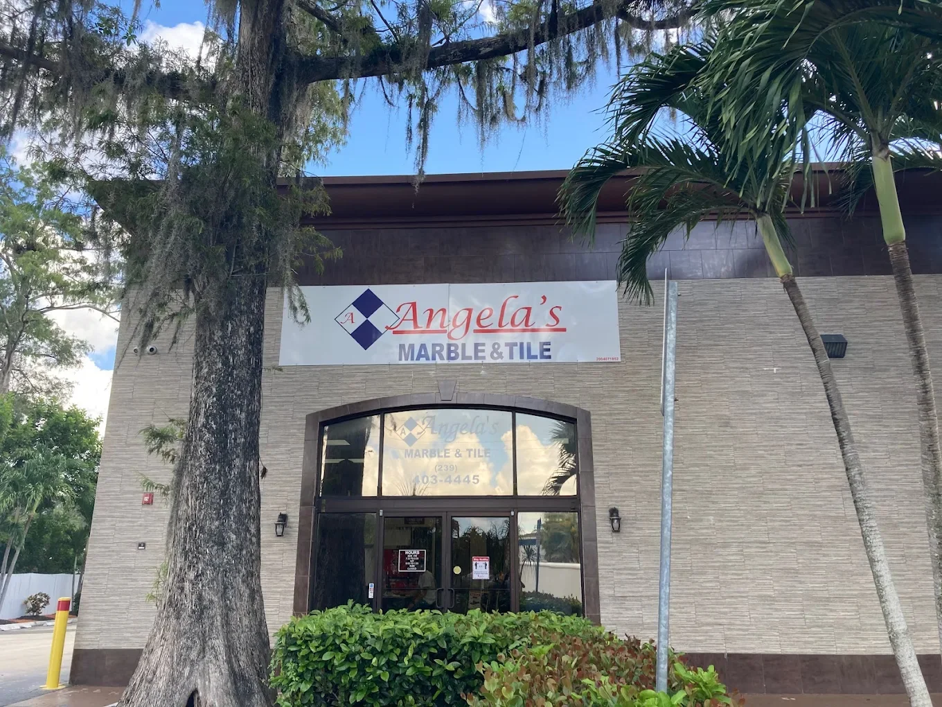 Front view of Angela's Marble & Tile store with trees and bushes outside