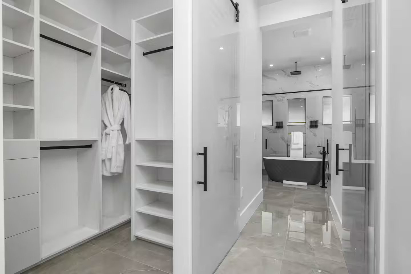 A walk-in closet leading to a modern bathroom with a black bathtub and marble walls.