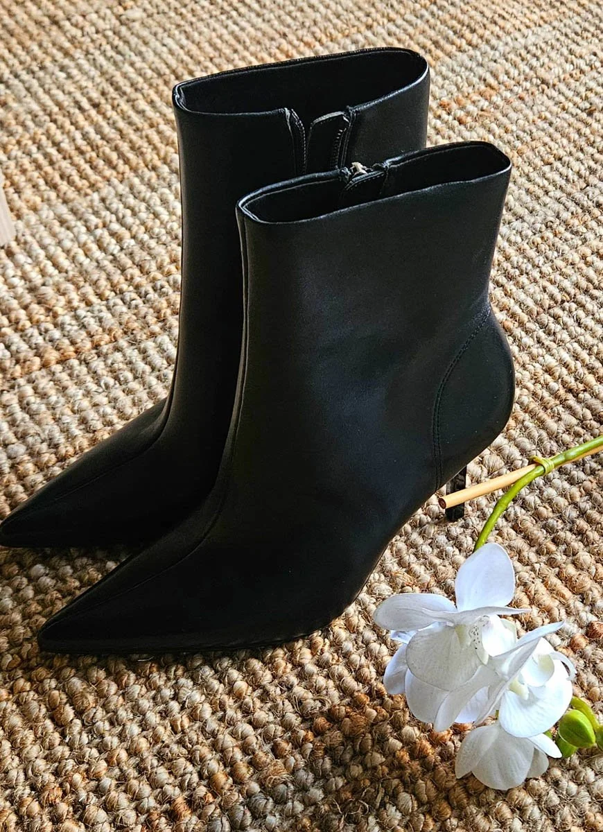 Mustat korkeakorkoiset saappaat lattialla, sivulta katsoen, pehmeällä matolla, ja valkoinen orkidea kukka näkyy edessä.