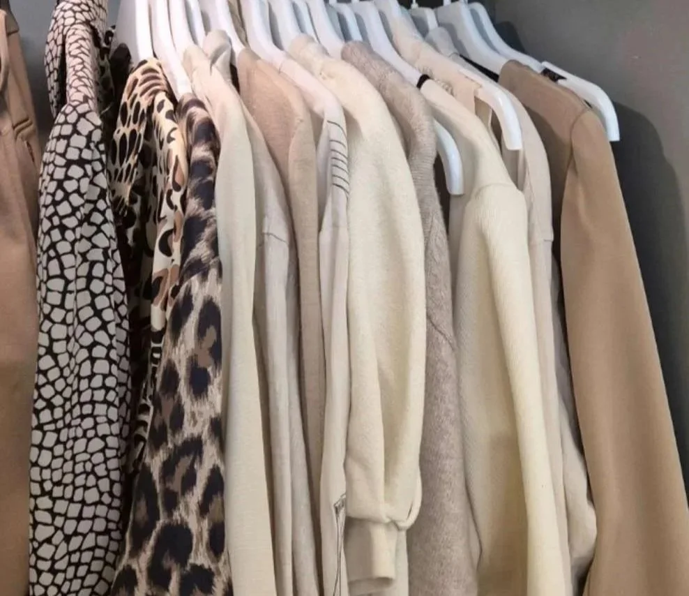 Neutraalivärisiä puseroita ja takkeja ripustettuna vaaterekissä.