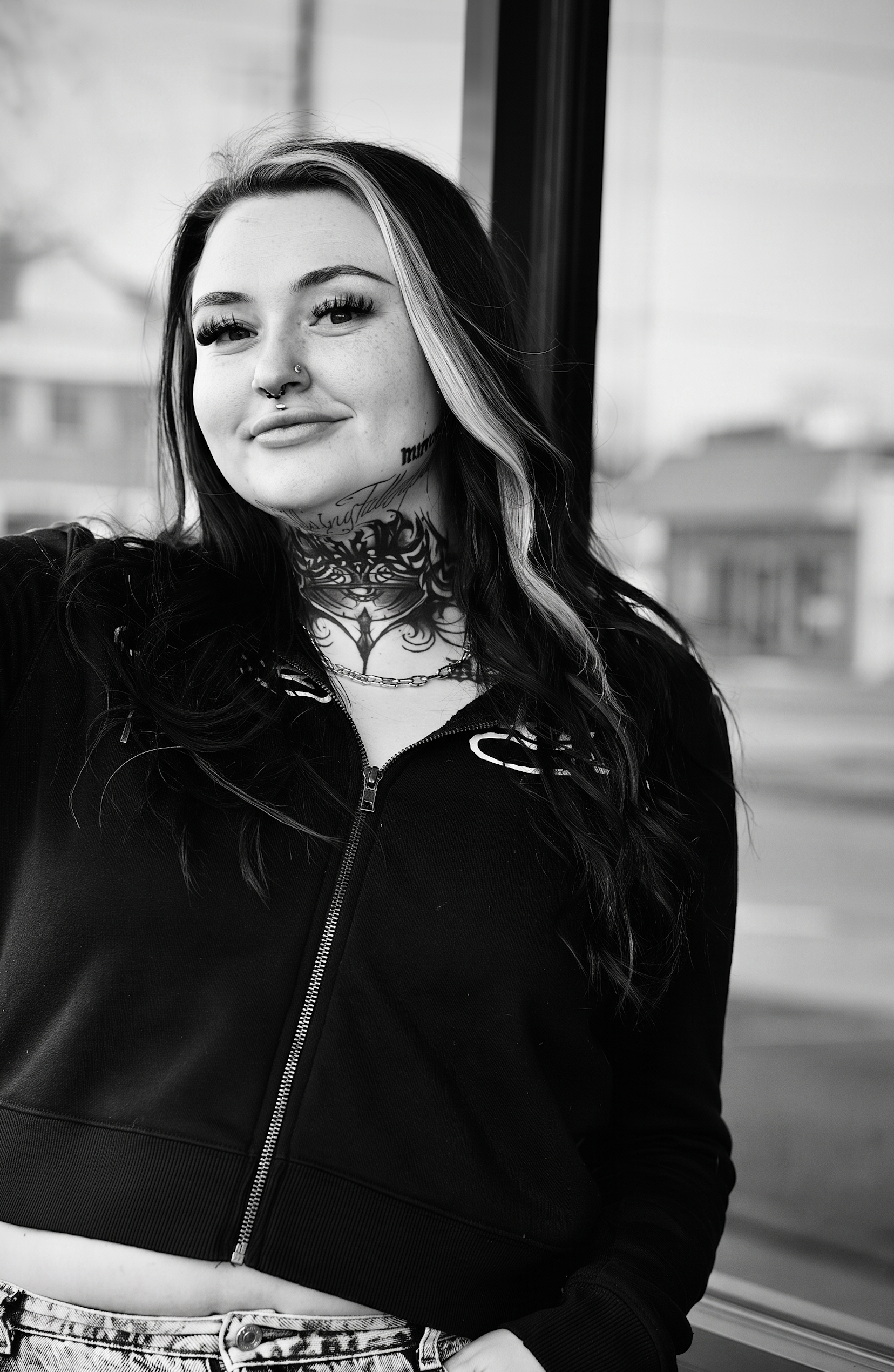 Black and white portrait Sydney Rose of SourPatchTatza, a heavily tattooed female tattoo artist at The Inksmith & Co. Tattoo Shop and Art Collective in Prineville, Oregon wearing a black zip-up hoodie.