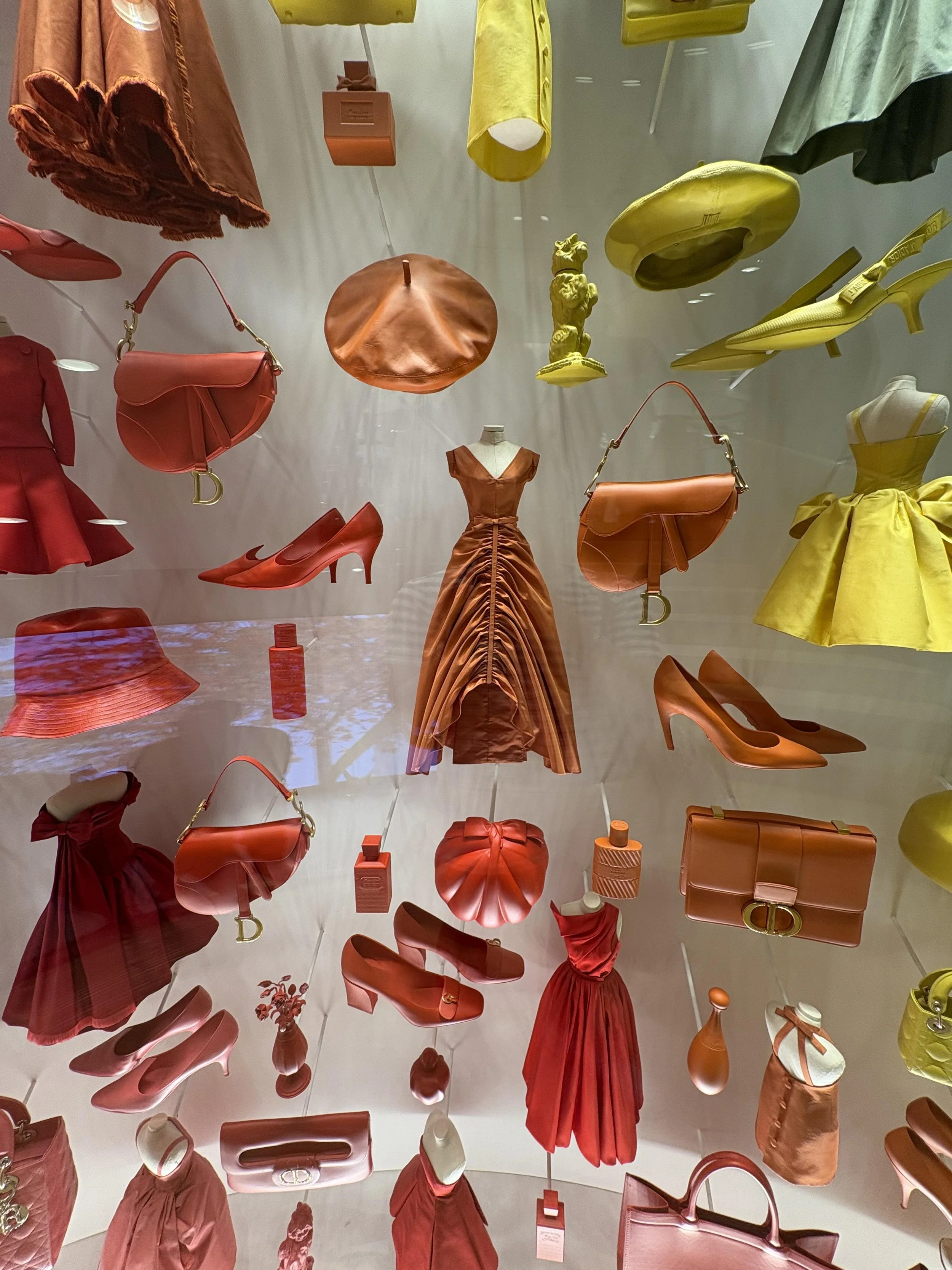 Display window with various fashion items including shoes, handbags, dresses, and accessories in shades of red, orange, and yellow.