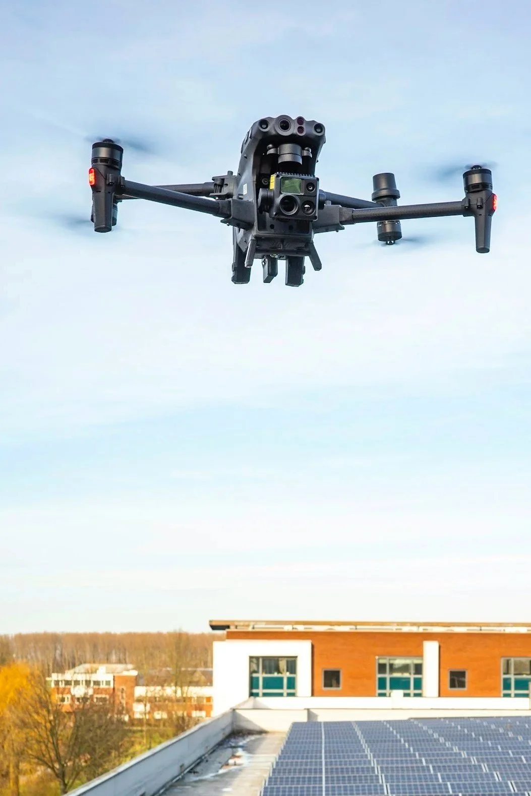 A drone flying in the sky above a building inspecting solar panels on the roof.