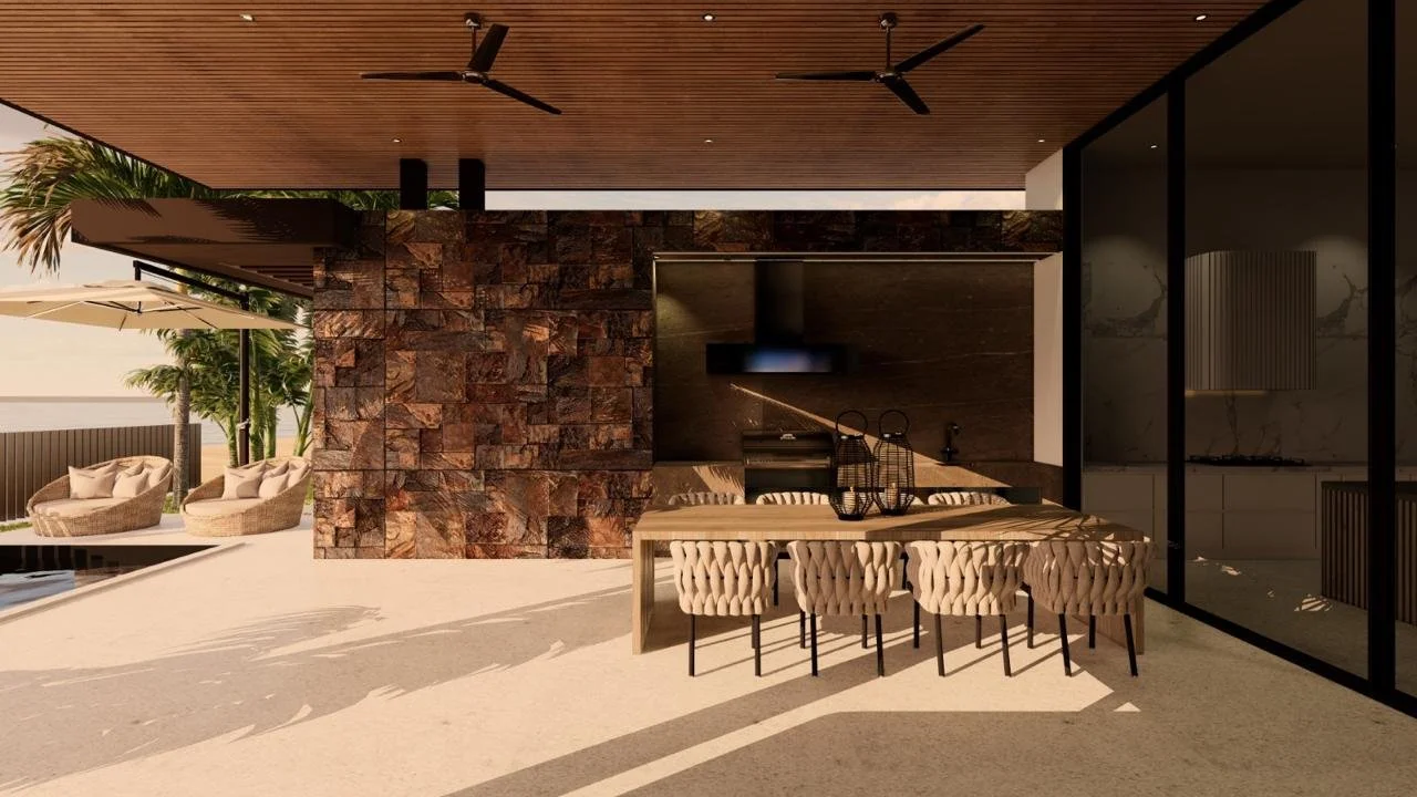 Espacio exterior de una casa moderna con área de comedor, barra con sillas, muro de piedra, sillones con cojines, sombrilla y árboles en un ambiente soleado.