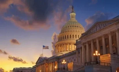 Vista del Capitolio de Estados Unidos al atardecer, con cielo colorido y bandera ondeando en la cima.