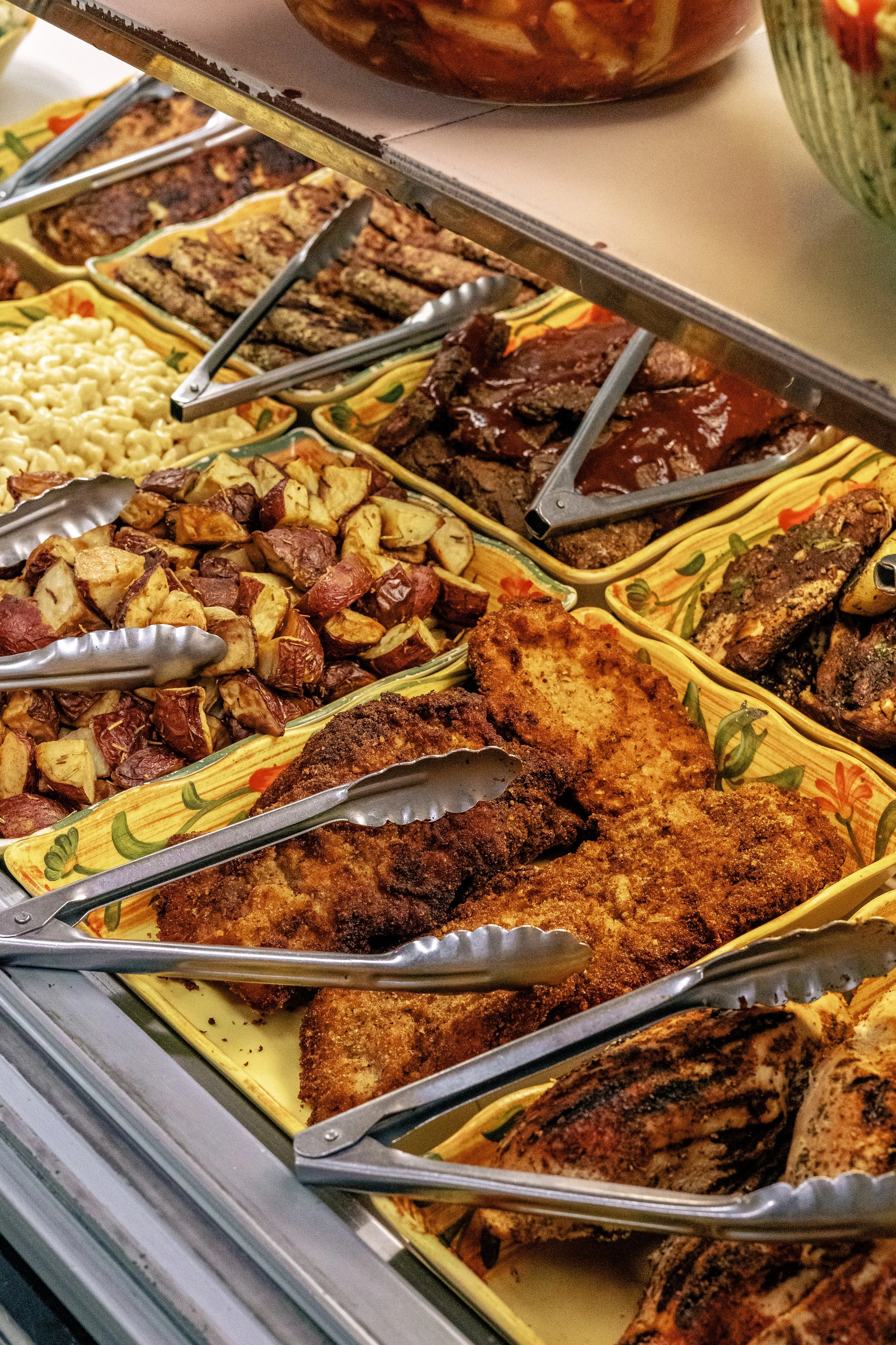 A buffet with fried fish filets, roasted potatoes, beef ribs, mac and cheese, and grilled vegetables.