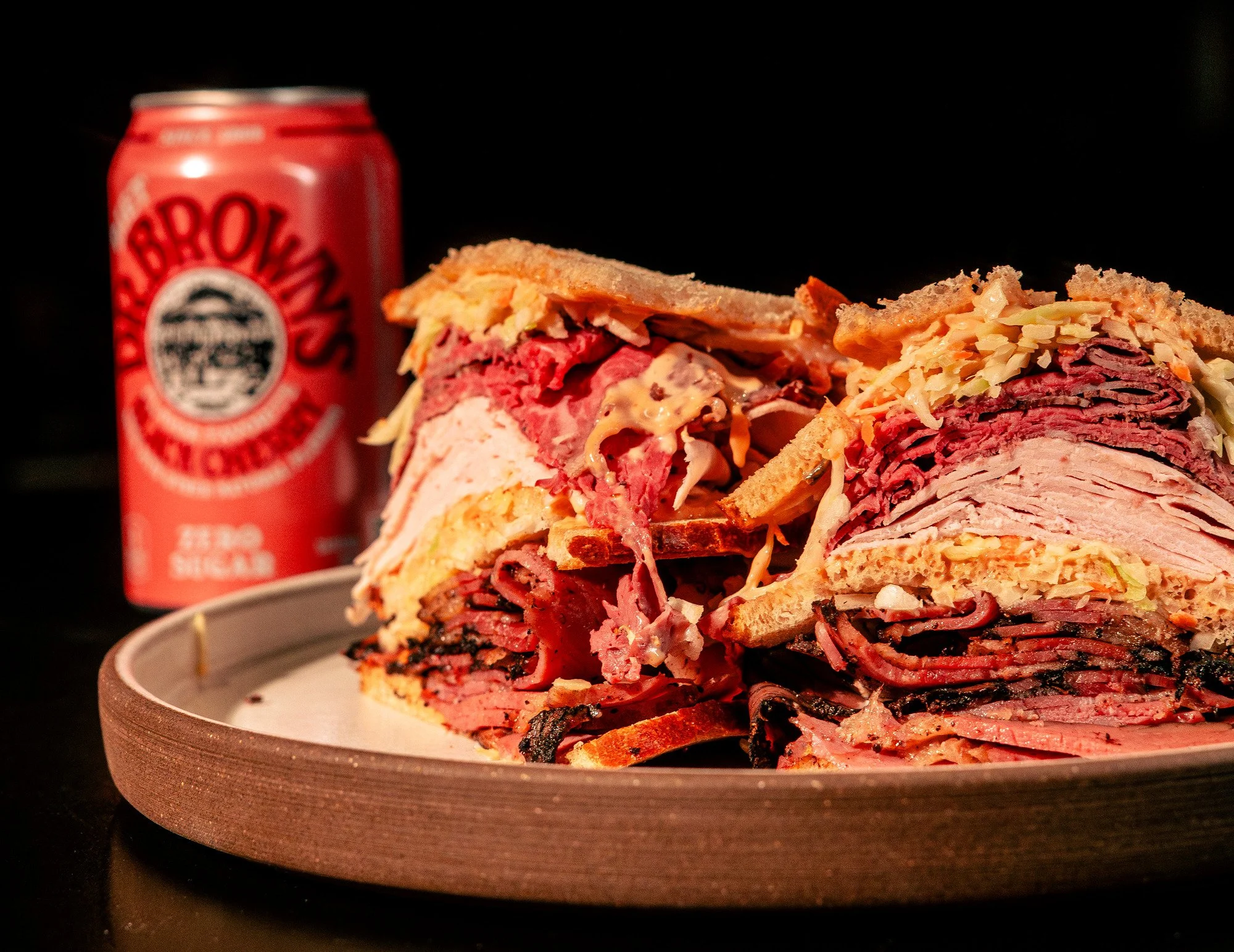 A plate with a large, sliced deli meat sandwich and a can of Detroit's famous cherry soda in the background.