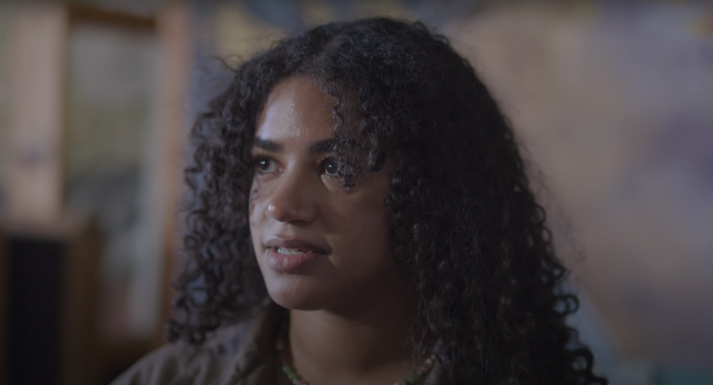A woman stands in a dark room with a concerned look on her face.