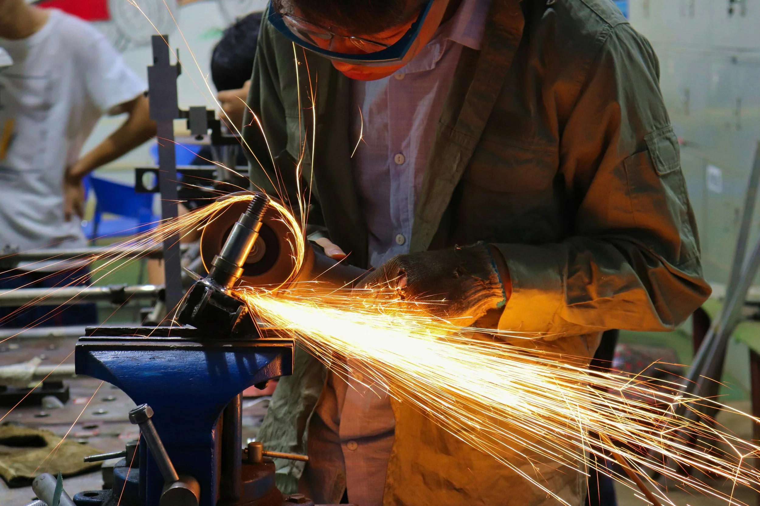 Person wearing safety glasses and gloves using a power grinder, producing sparks.