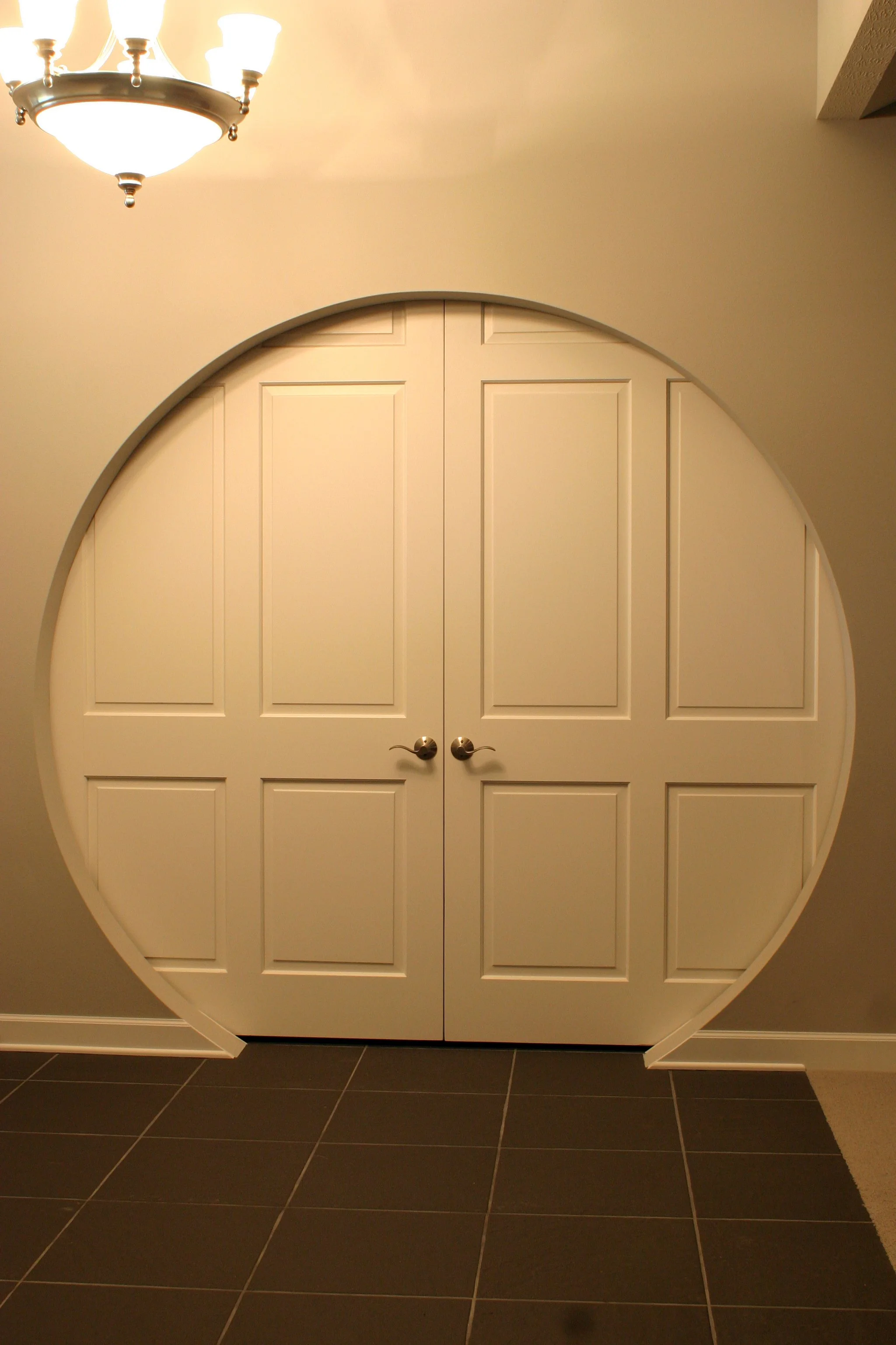 Double white doors with a circular cutout, located in a room with a tiled floor, under a ceiling with a light fixture.