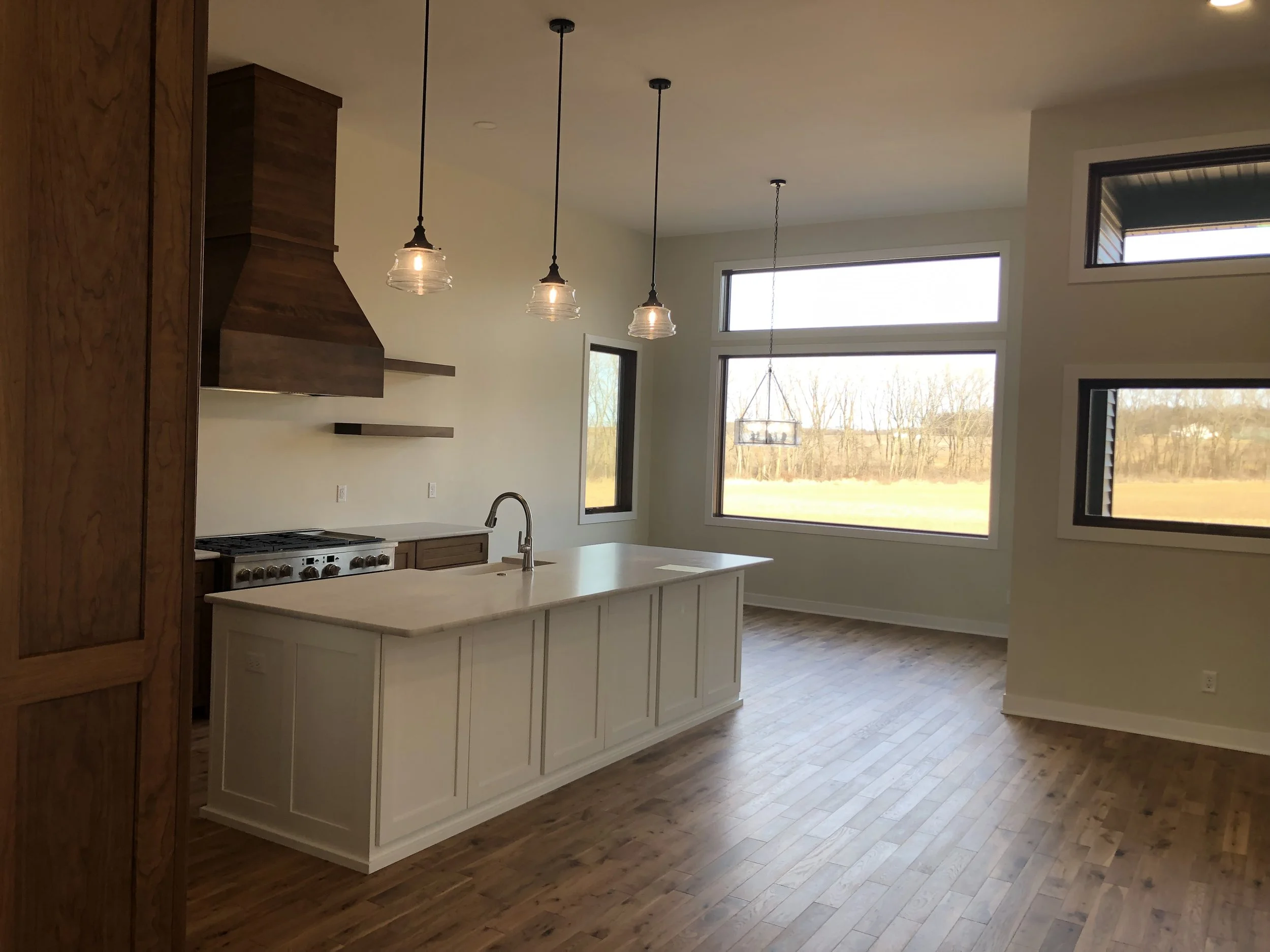 Empty modern kitchen with island, hardwood floors, large windows, and wood accents.