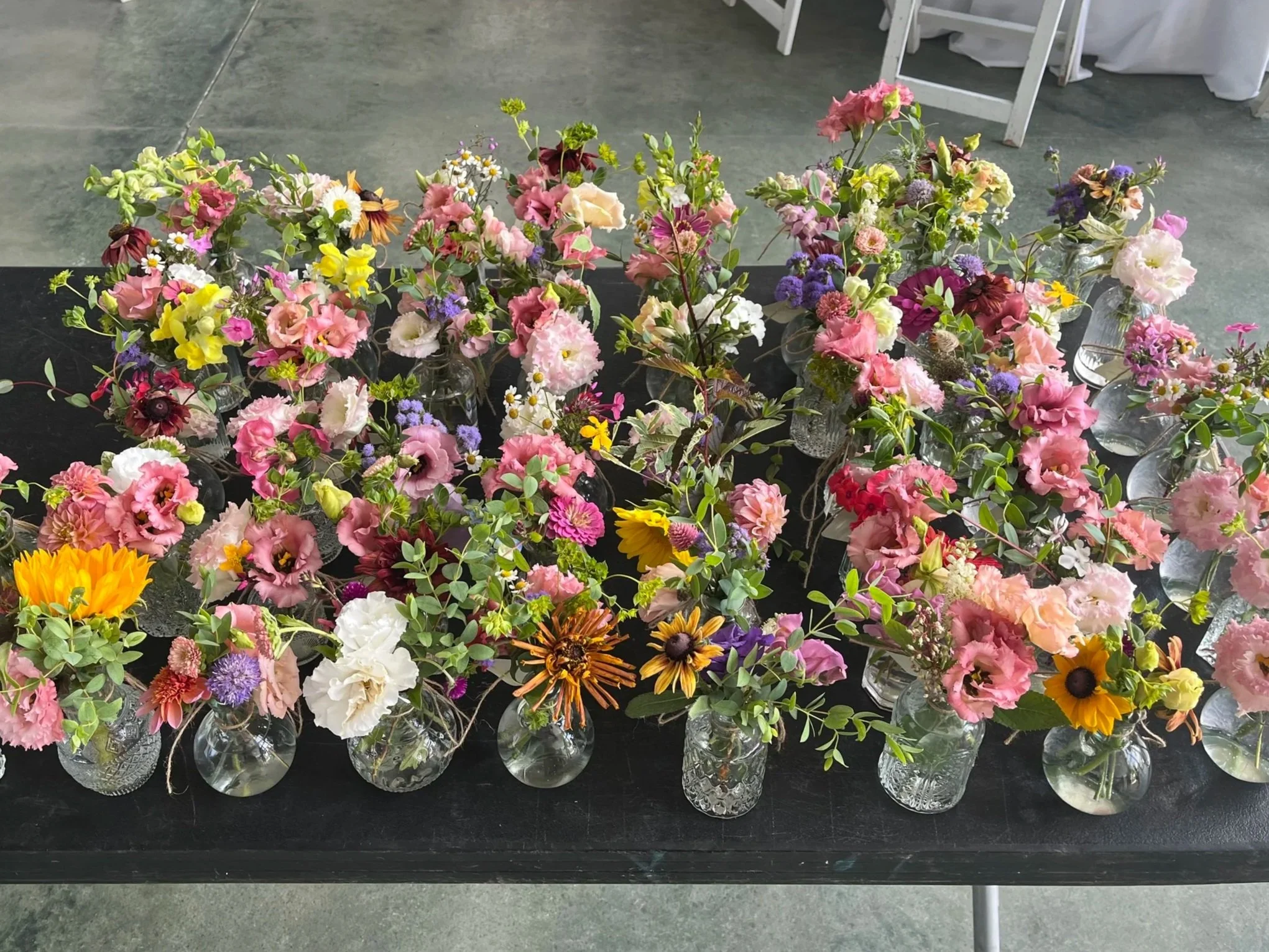 A display of multiple glass vases filled with colorful fresh flowers on a black table at an indoor event.