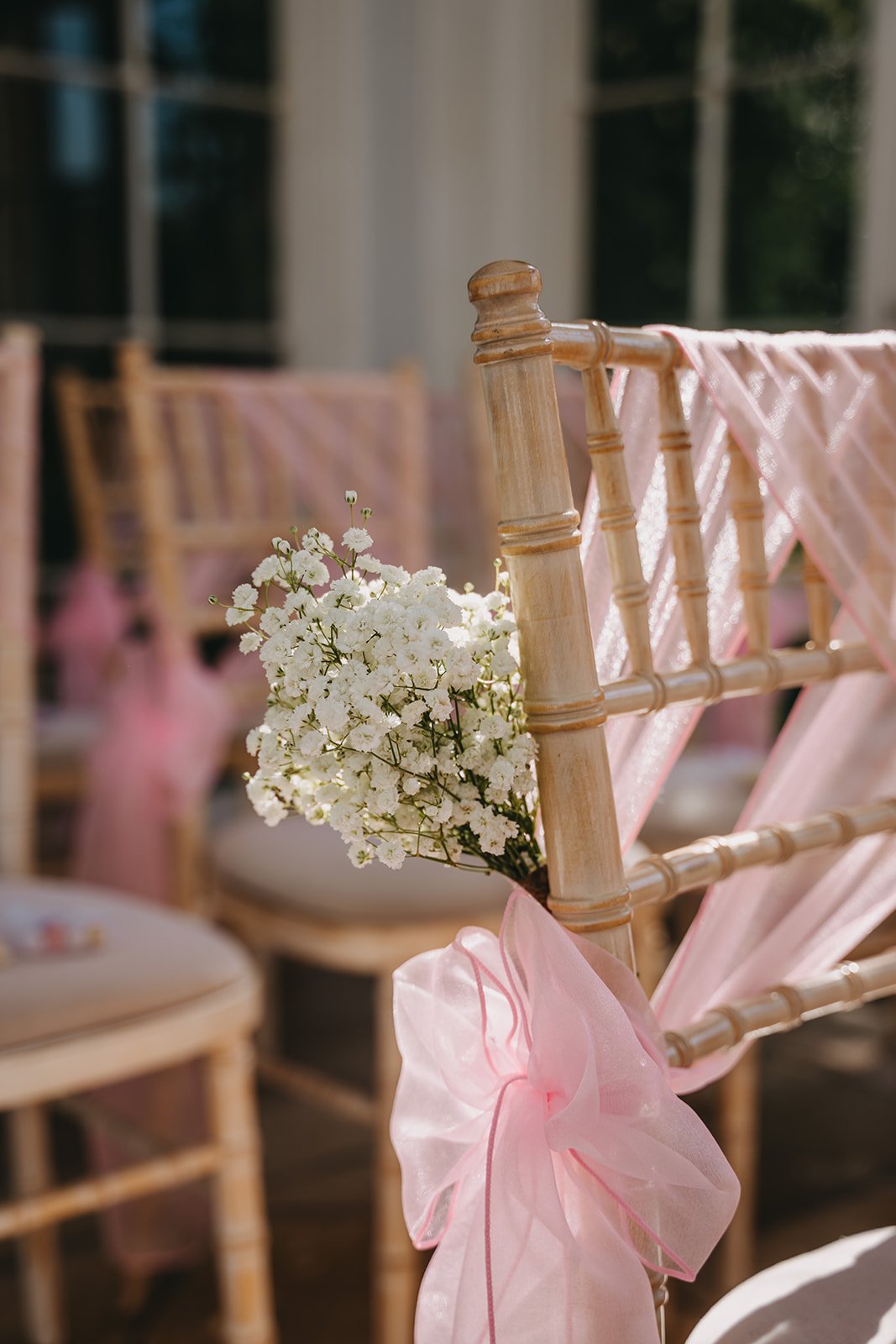Wooden chair decorated with pink fabric and white flowers at an outdoor event.