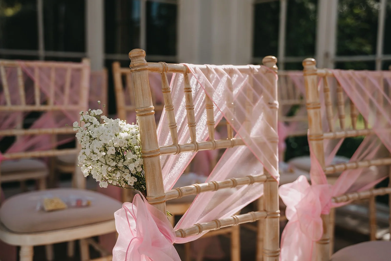 Close-up of decorated chairs with pink tulle and white flowers at an outdoor wedding or event