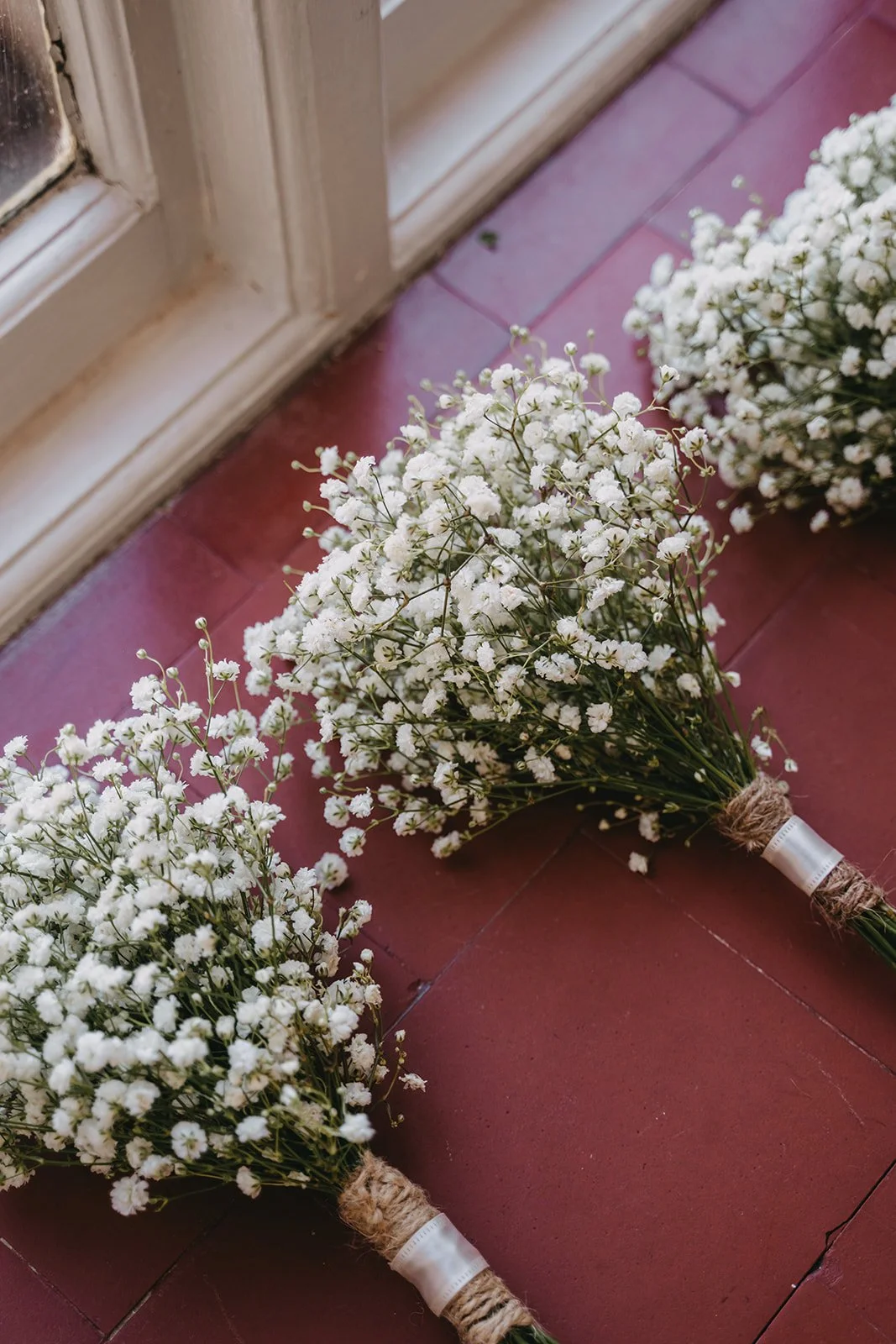 Two bouquets of white baby's breath flowers on a red floor, near a glass door.
