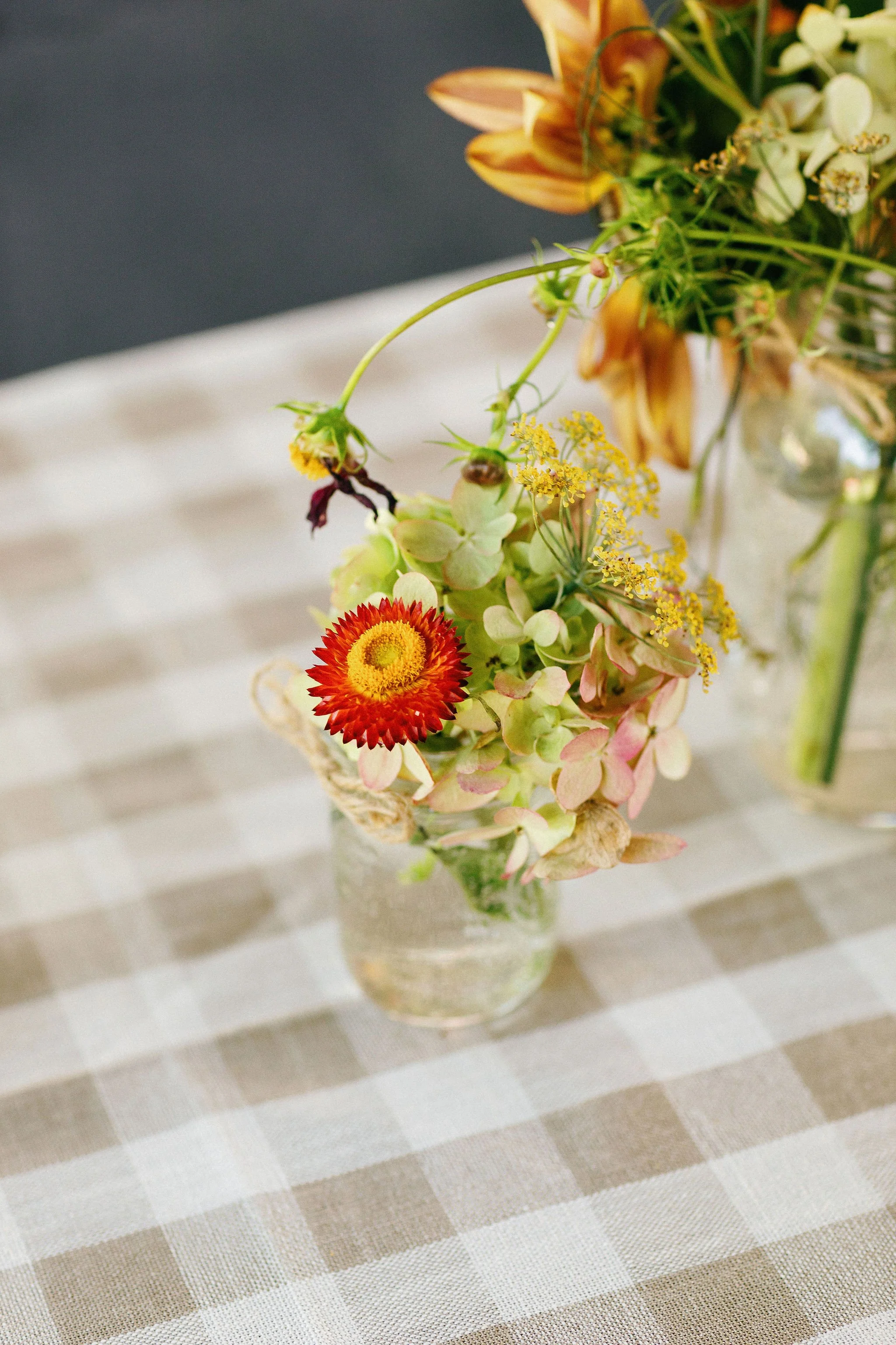 Small glass vase with a bouquet of assorted flowers on a checkered tablecloth.