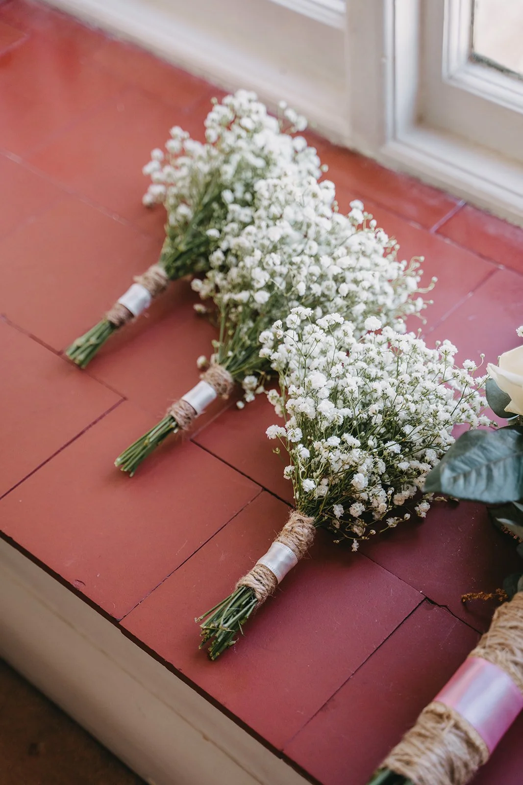 Three small bouquets of white baby's breath flowers on a red wooden surface near a window.