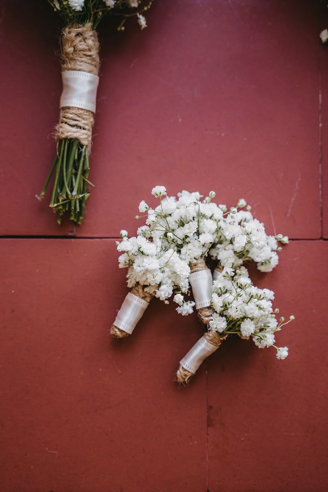 Bouquets of white baby's breath flowers wrapped with twine and white tape, placed on a reddish-brown tiled floor.