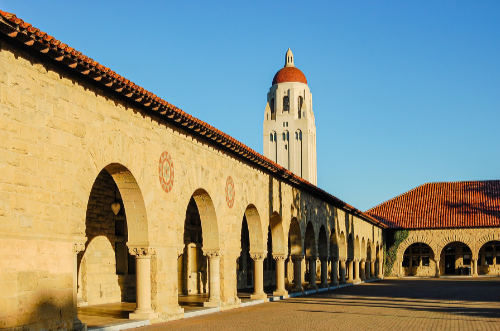 Historic stone building with arches and a tall clock tower against a clear blue sky.